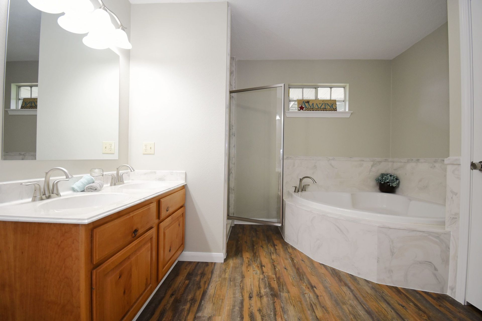 Bathroom with a double vanity, shower, and soaking tub; wood-look flooring.