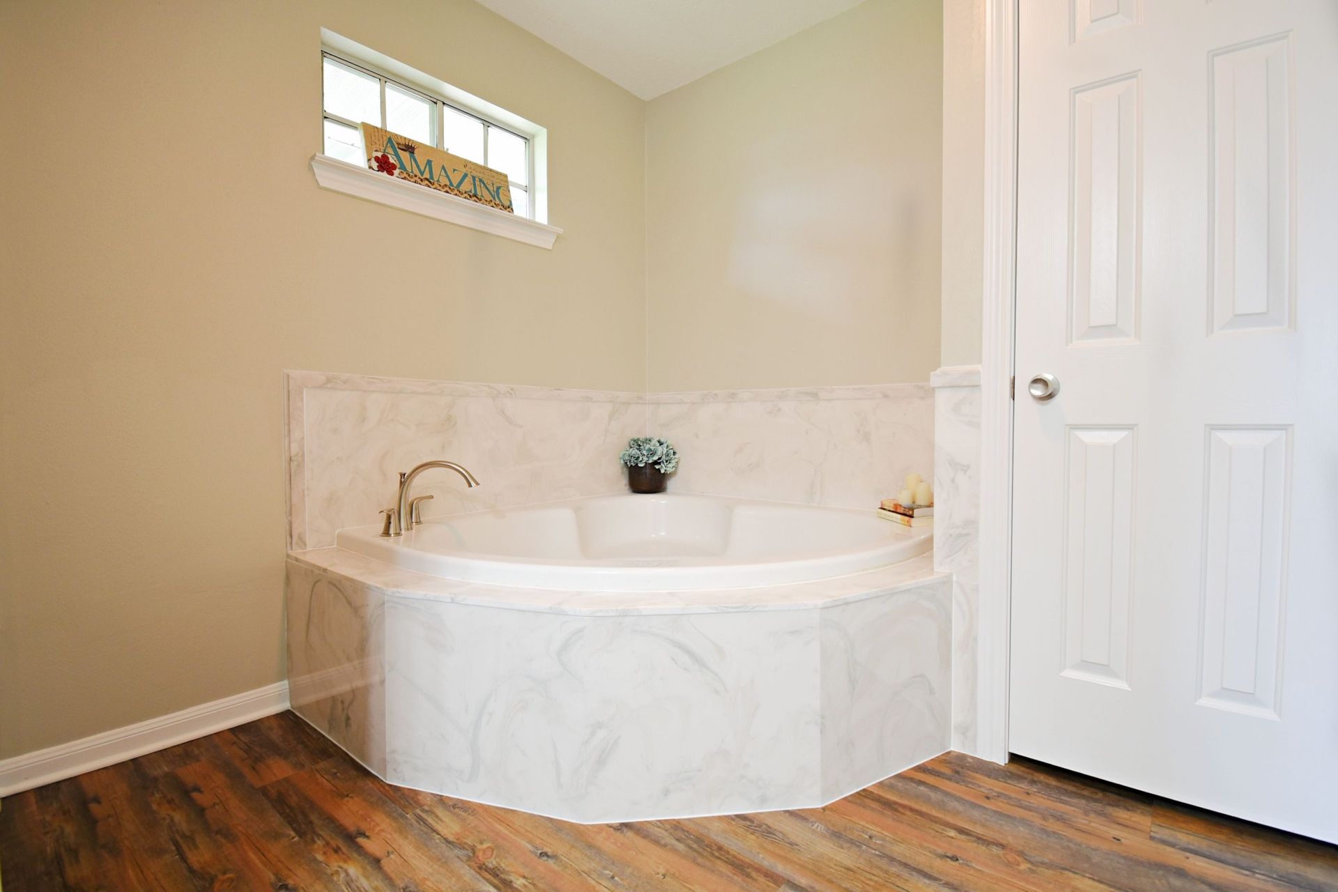 Bathroom with a corner jacuzzi tub, white marble and floral decor, with a window and a closed white door.