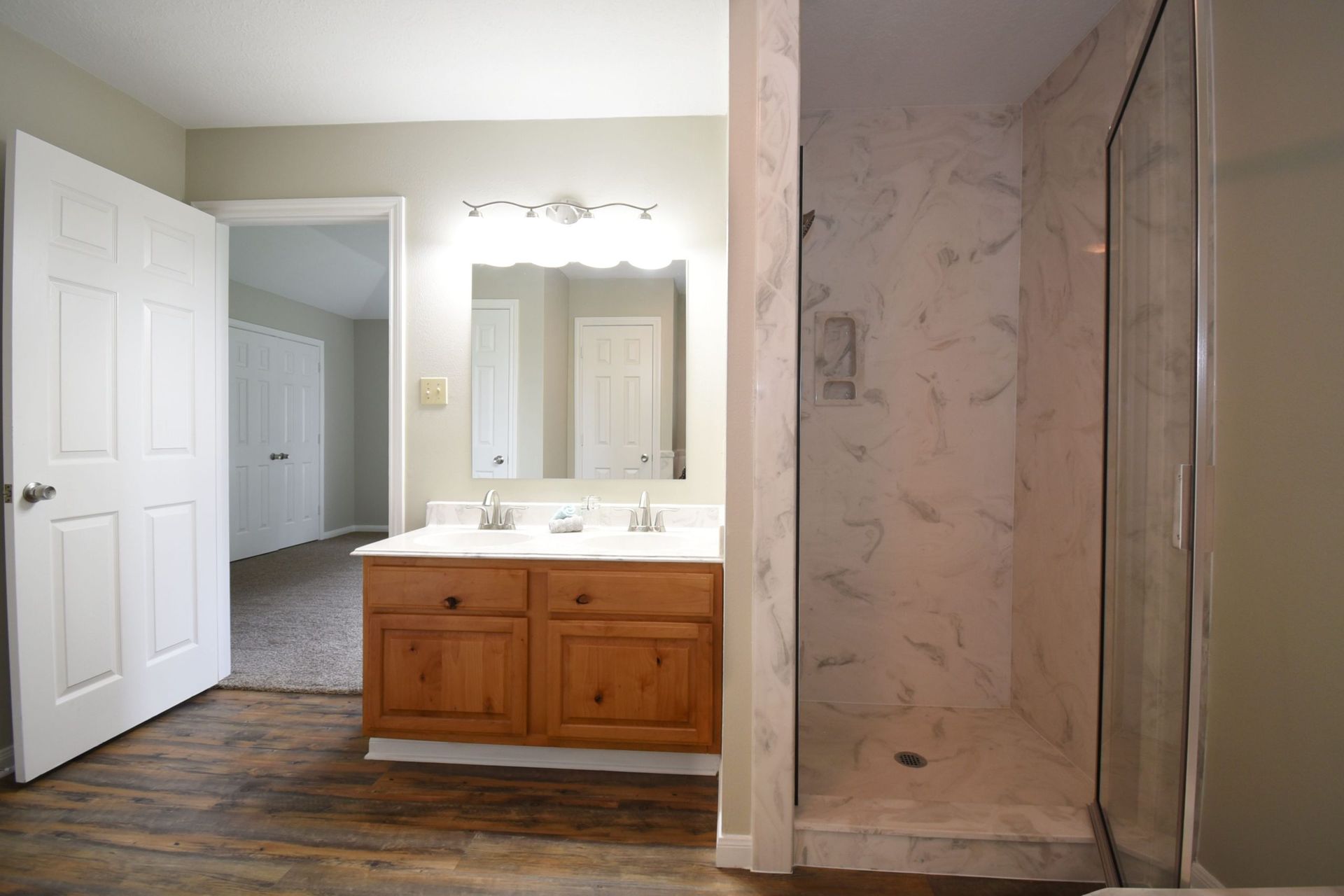 Bathroom with a vanity, walk-in shower, and open door leading to a hallway.