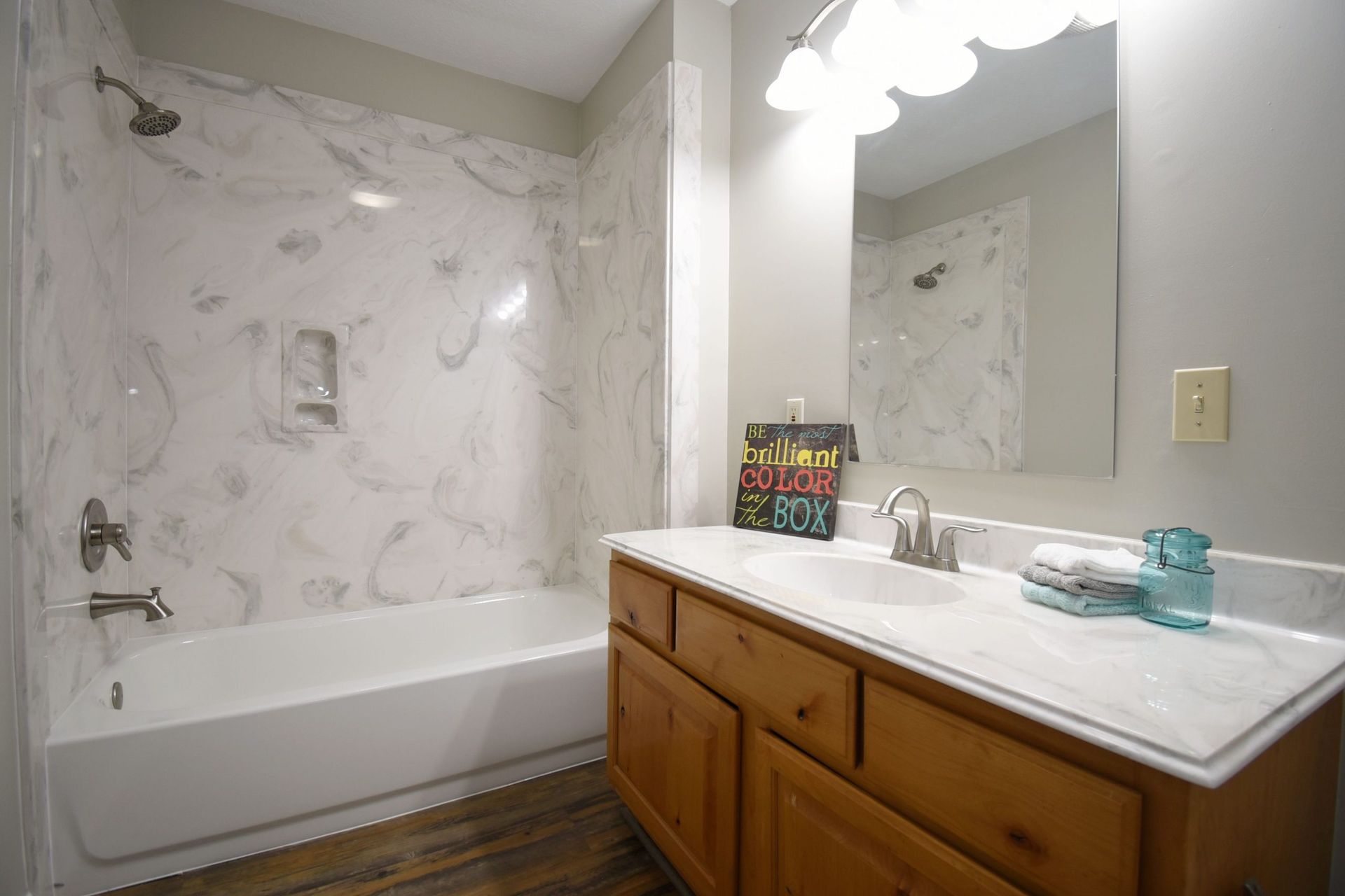 Bathroom with marble-look shower surround, light wood vanity, and a mirror.