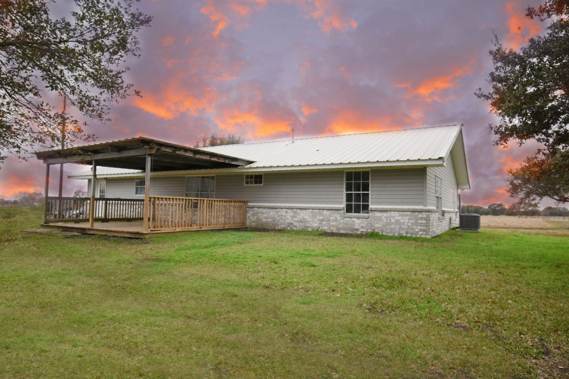 Ranch-style home with porch on a grassy lot under a vibrant sunset.