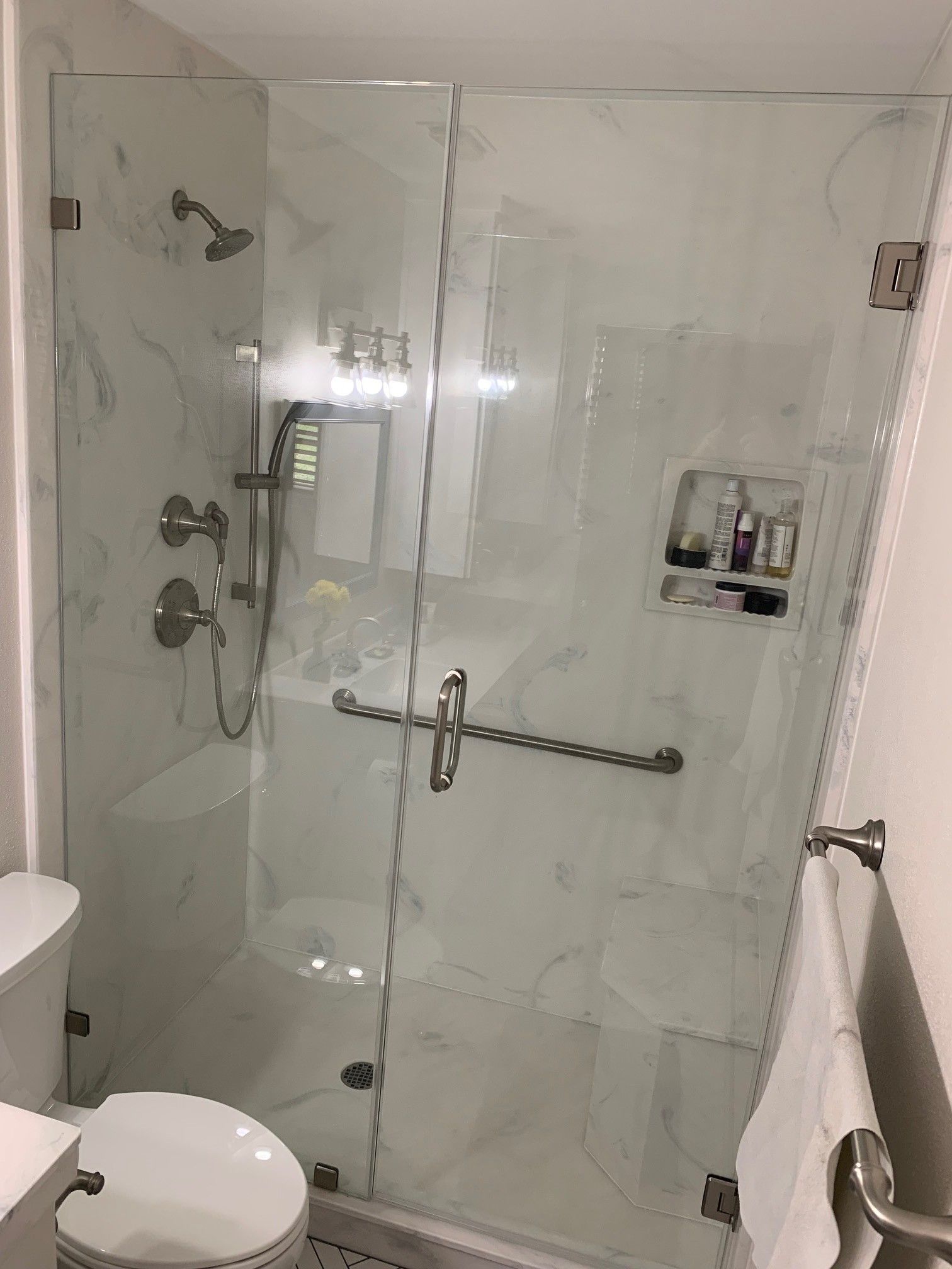 A modern, marble-tiled shower with glass doors, shower fixtures, and a towel rack.