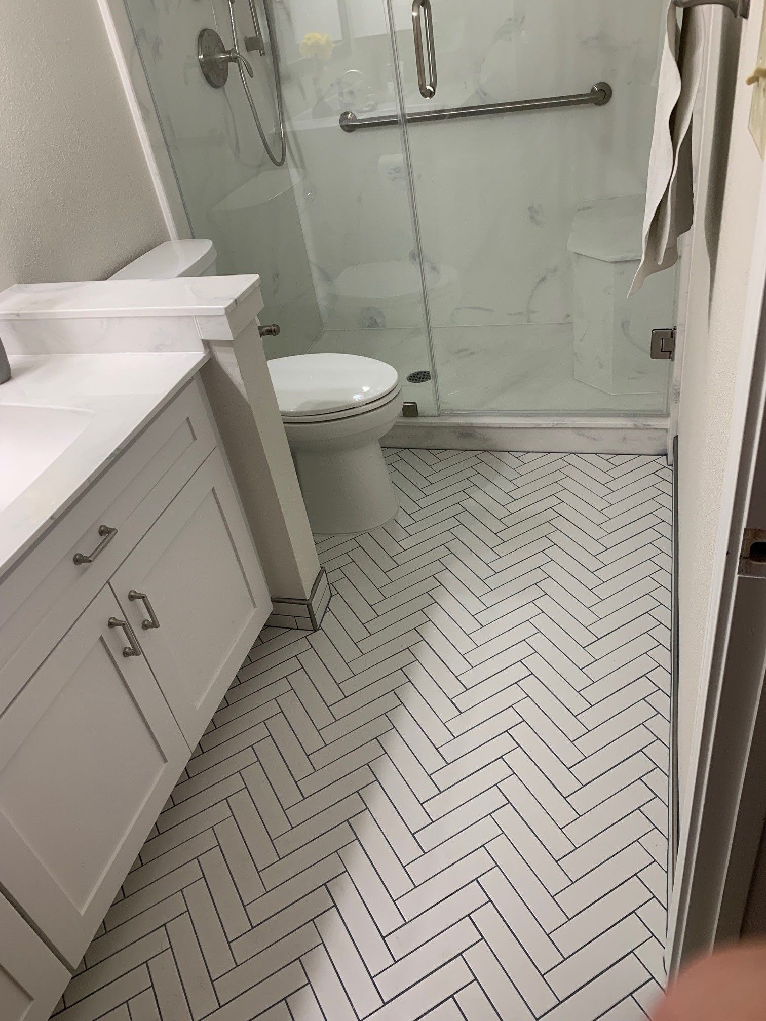 Bathroom with white cabinets, toilet, and shower. Herringbone-patterned white and black floor tiles.