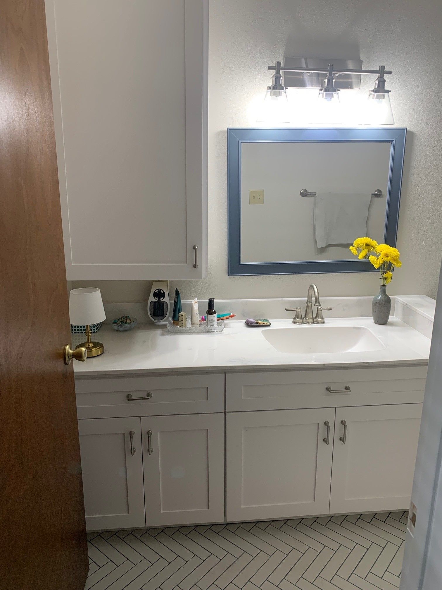 White bathroom with a blue-framed mirror, white cabinets, and yellow flowers.
