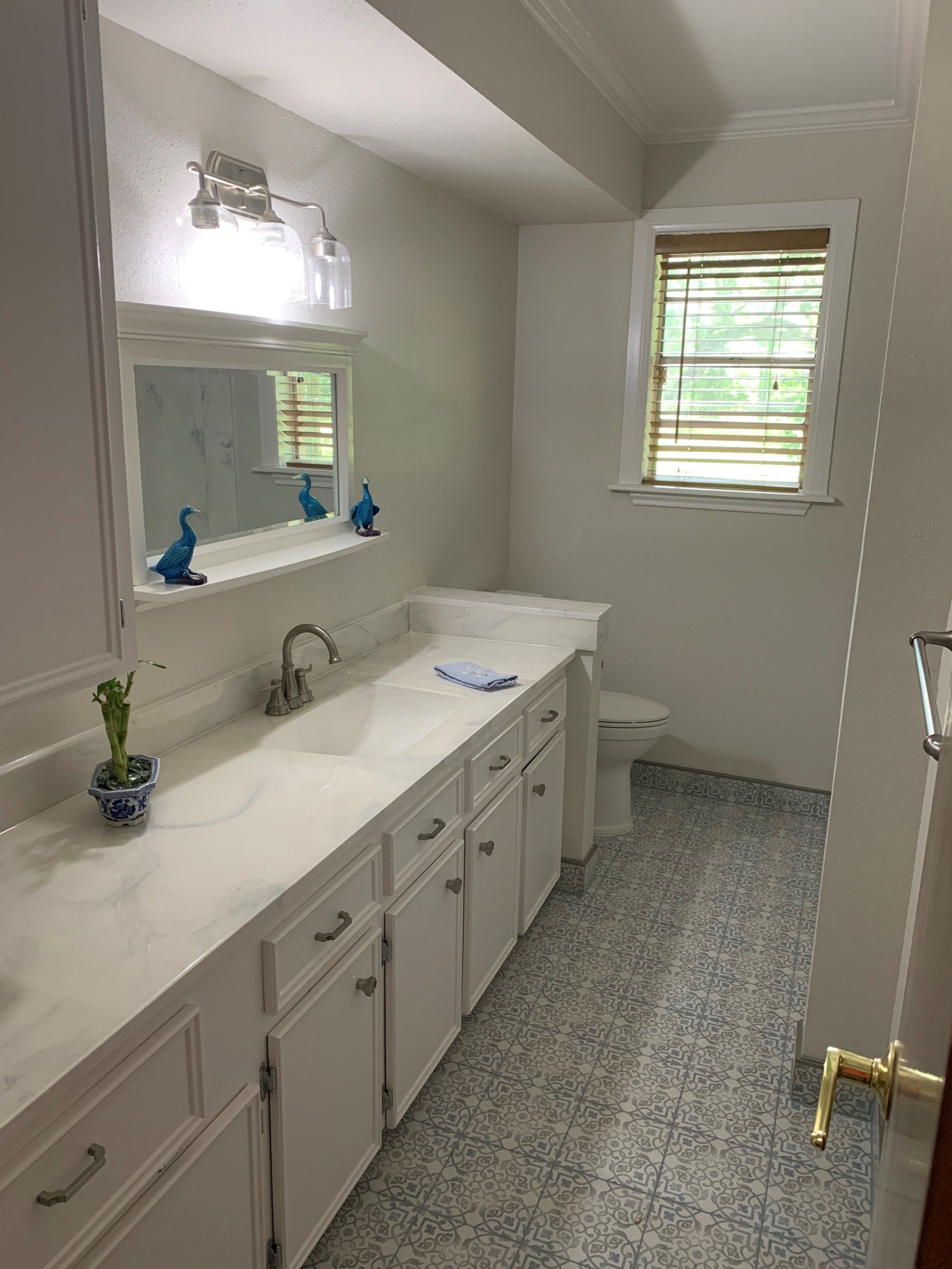 White bathroom with long vanity, mirror, window, and patterned blue floor.