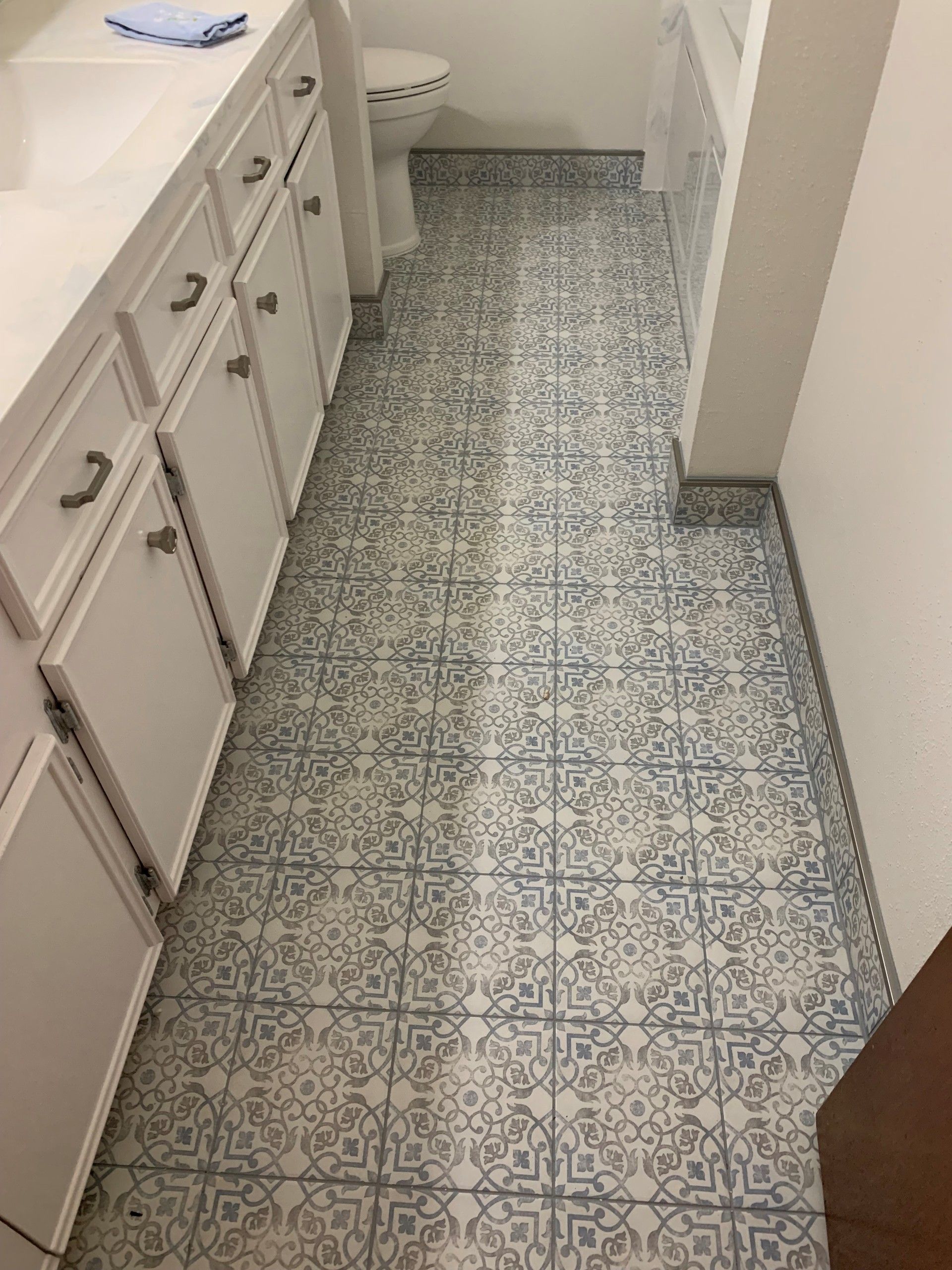 Bathroom floor with blue and white patterned tiles, white cabinets, and a toilet.