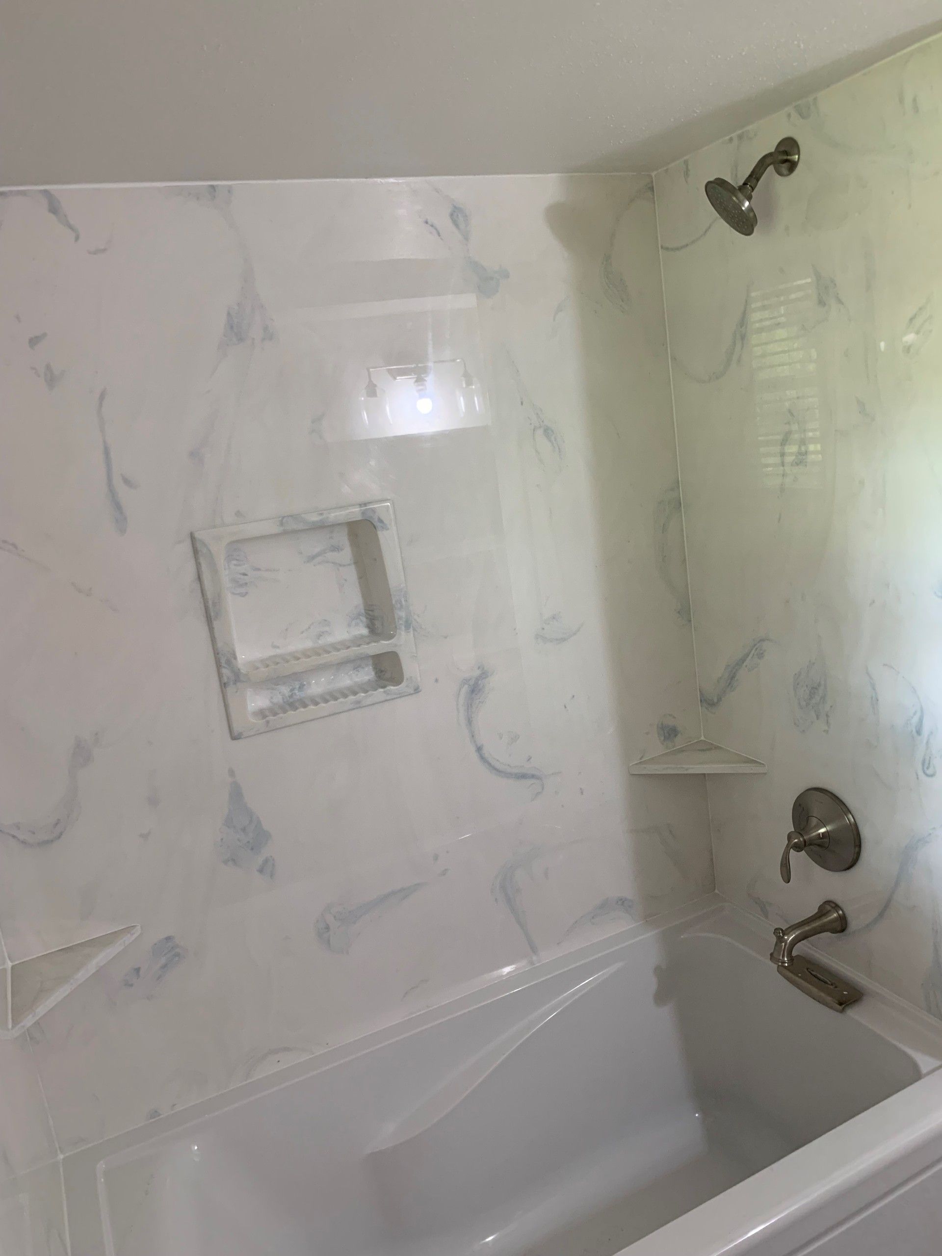 White and blue marbled-patterned shower and tub combo with a built-in shelf and shower fixtures.