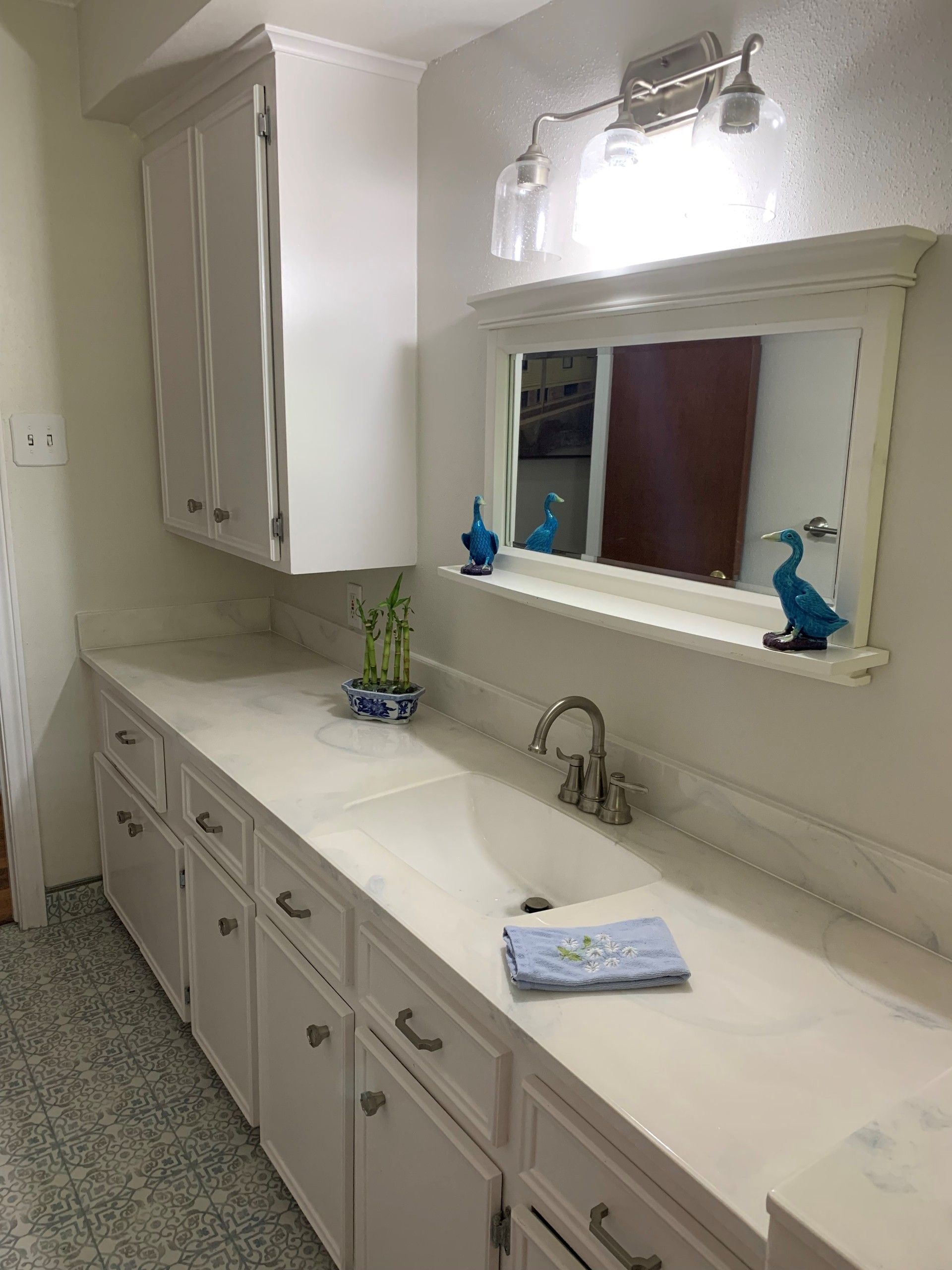 White bathroom with countertop, cabinets, mirror, and faucet. Blue accents.