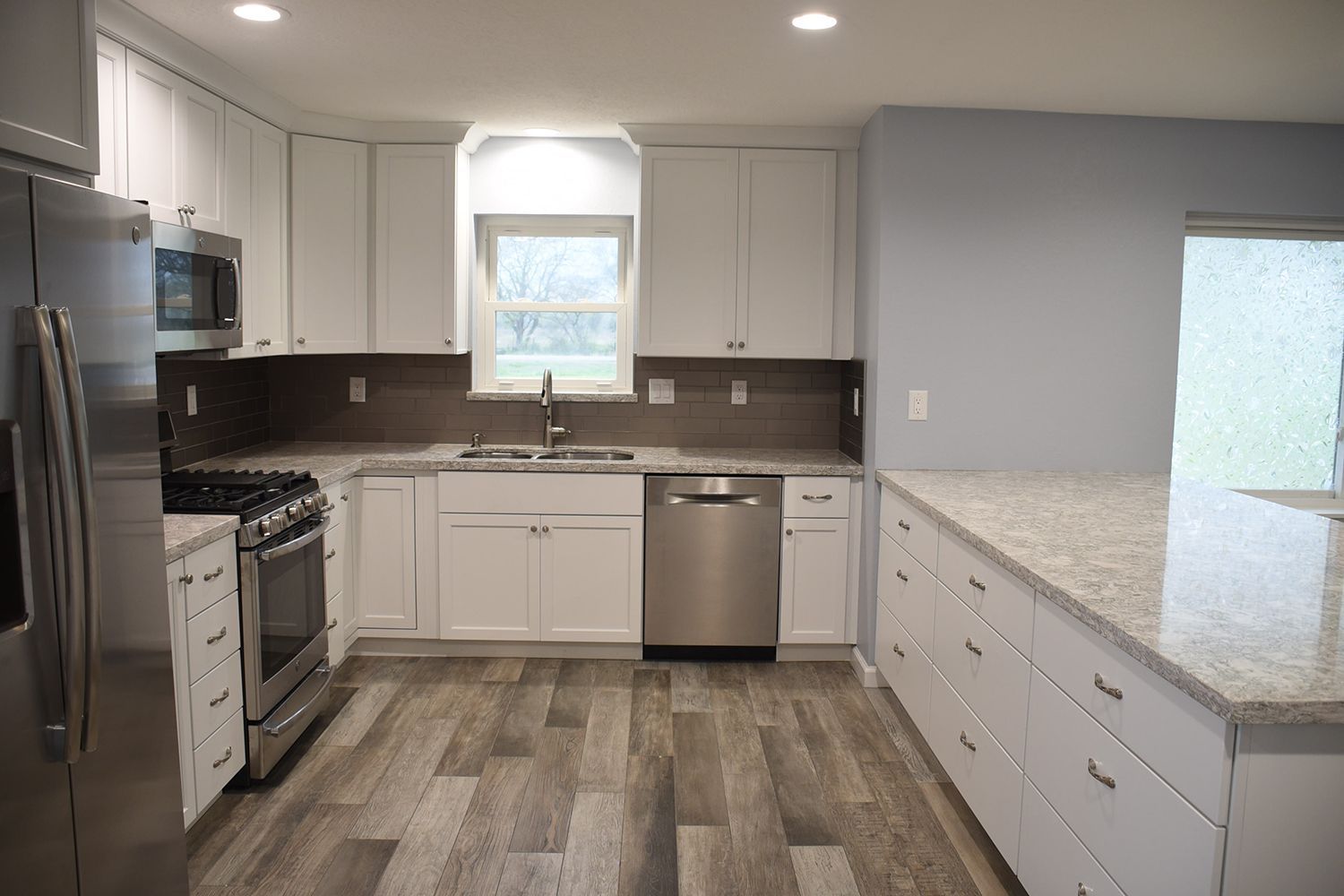 Modern kitchen with white cabinets, stainless steel appliances, and light gray countertops and backsplash.