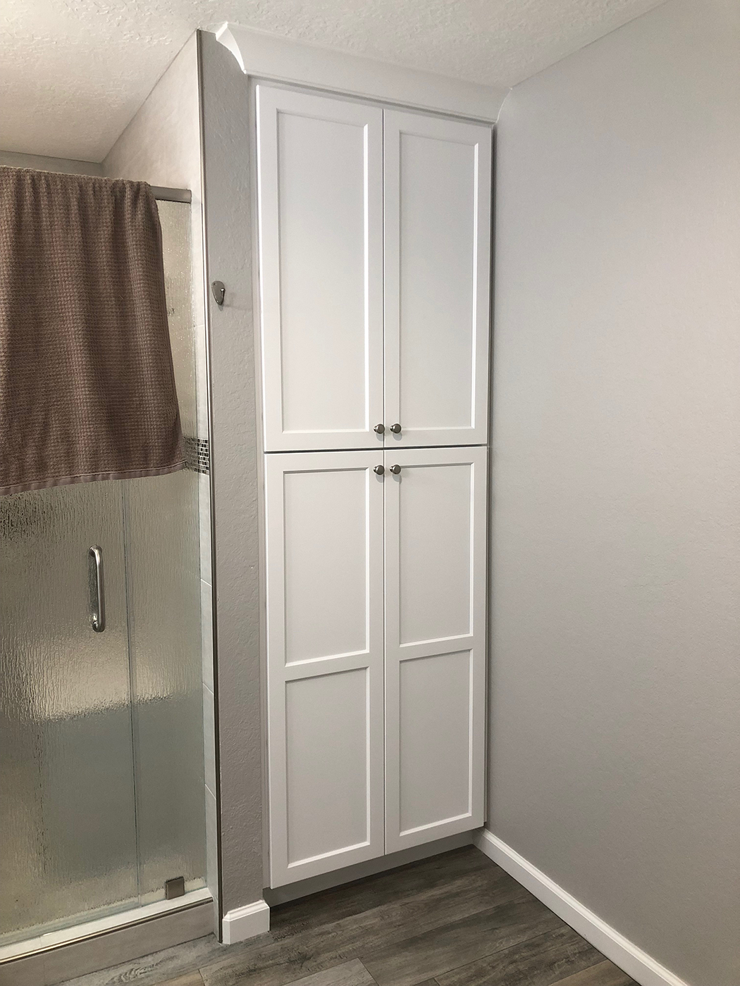 Tall white bathroom cabinet next to shower with glass door, in corner of the room.
