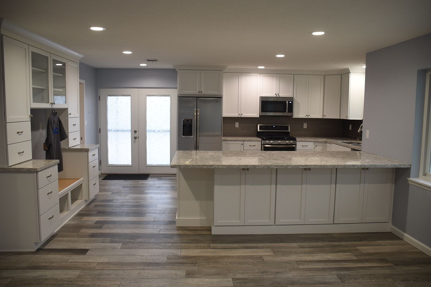 Spacious, modern white kitchen with island, cabinets, stainless appliances, and light wood flooring.