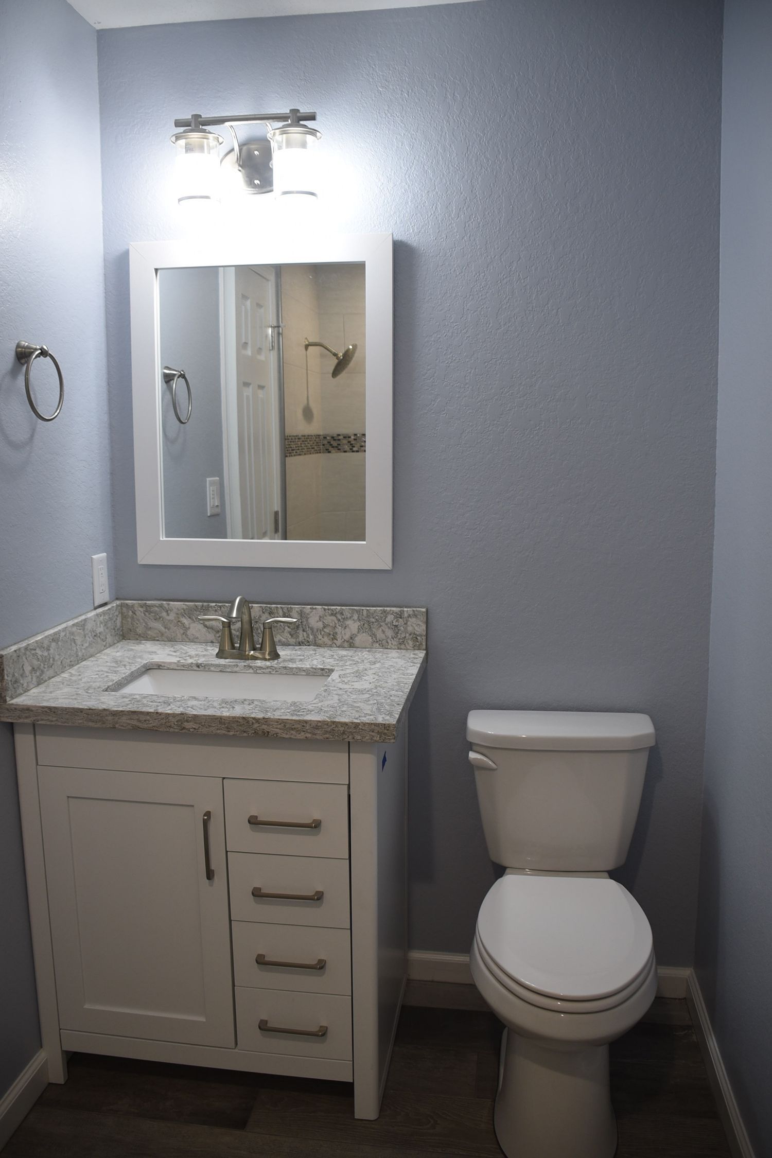 Small bathroom with white vanity, toilet, and mirror against blue textured walls.