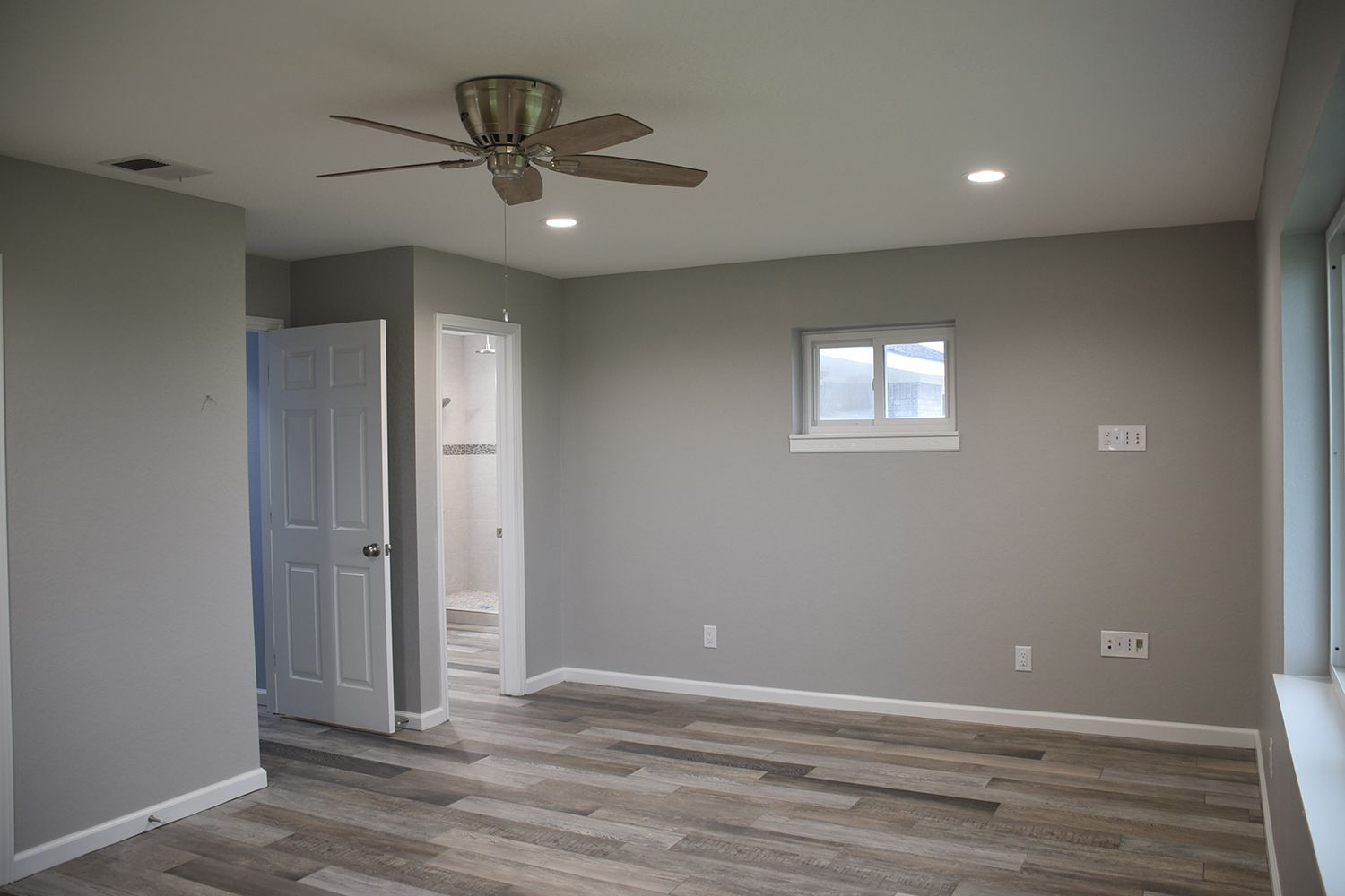 Gray-painted bedroom with wood-look flooring, white doors, ceiling fan, recessed lights, and a small window.