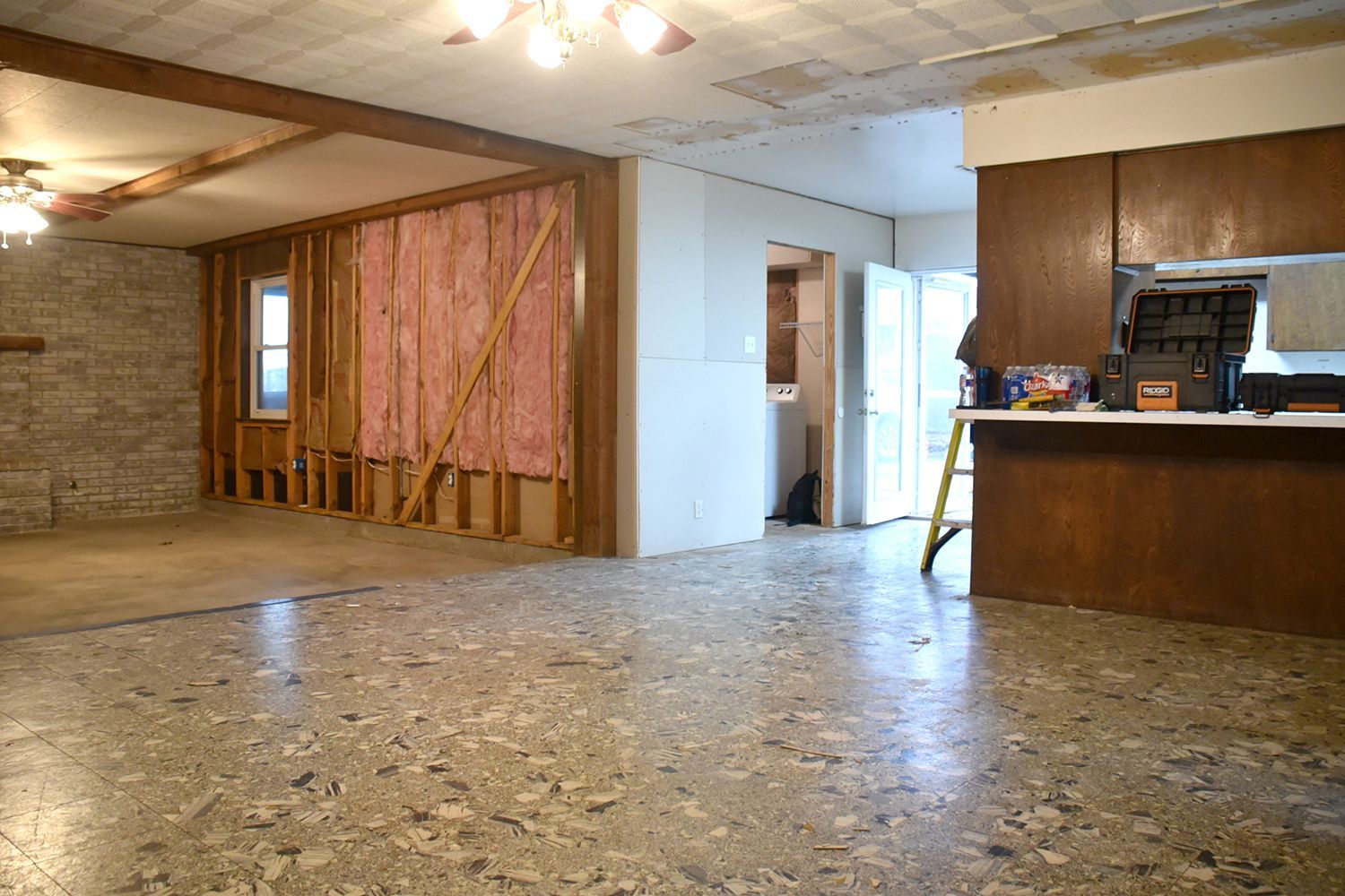Room undergoing renovation, exposed framing and insulation, concrete floor, wooden cabinets.