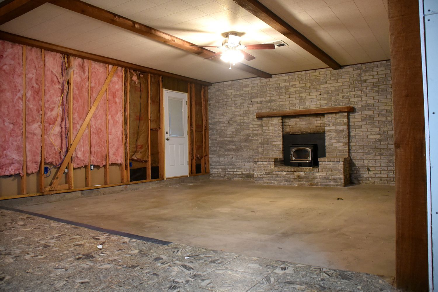 A room with exposed studs, insulation, a brick fireplace, and a concrete floor during renovation.