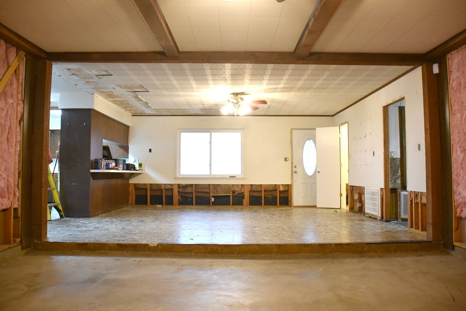 Interior view of a home under renovation; exposed walls and floors, showing kitchen and open doorway.