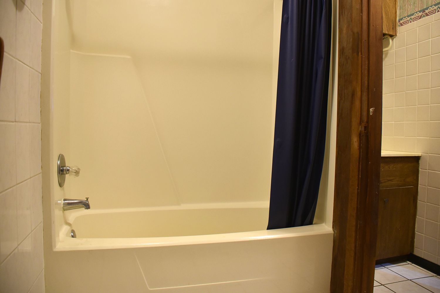 A plain, cream-colored bathtub with a blue shower curtain. A wooden support beam is on the right.