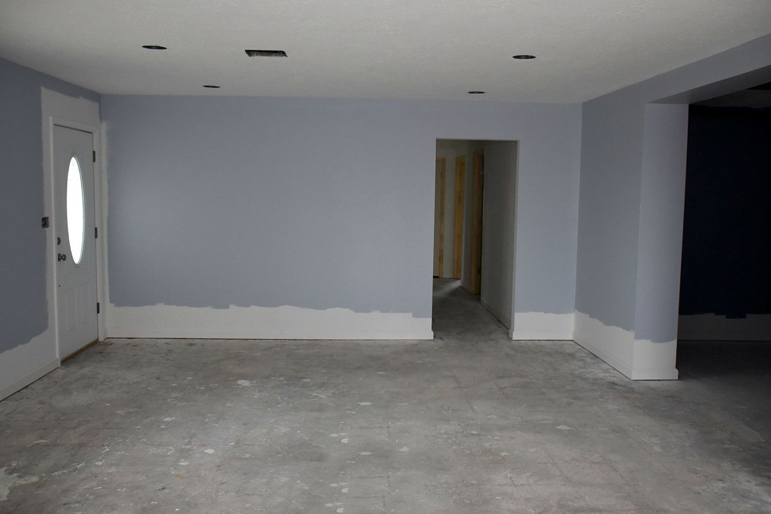 An empty room with blue-gray walls, white trim, a doorway, and a white door with a large oval window.