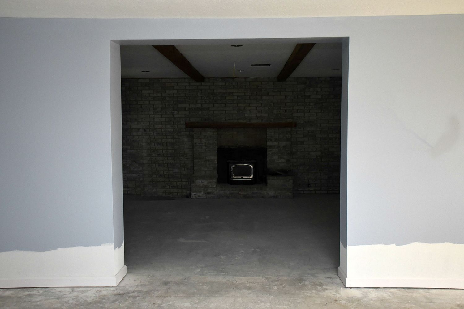 Interior doorway leading to a room with a fireplace and exposed brick wall; pale blue walls, white trim.