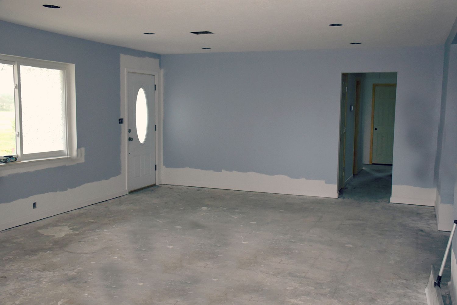 Empty room with light blue walls, white trim, and a gray concrete floor.
