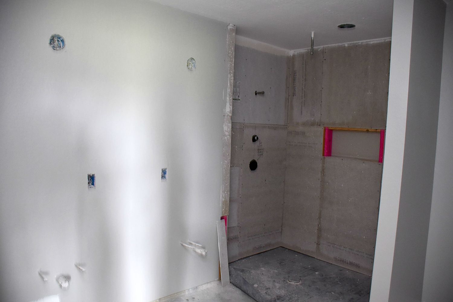 Bathroom under construction with drywall, unfinished shower area, electrical outlets visible.