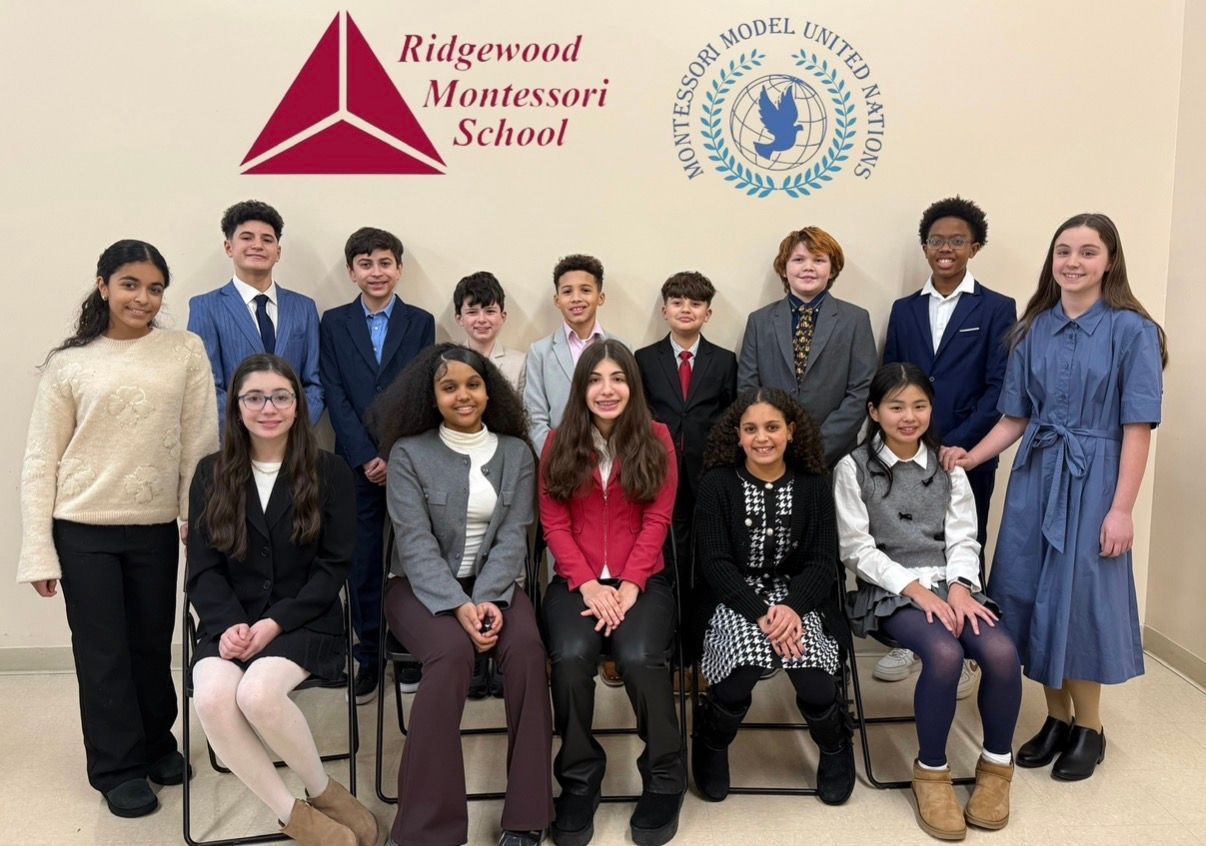 Group of students and staff posing indoors in front of a Montessori school logo and banner.