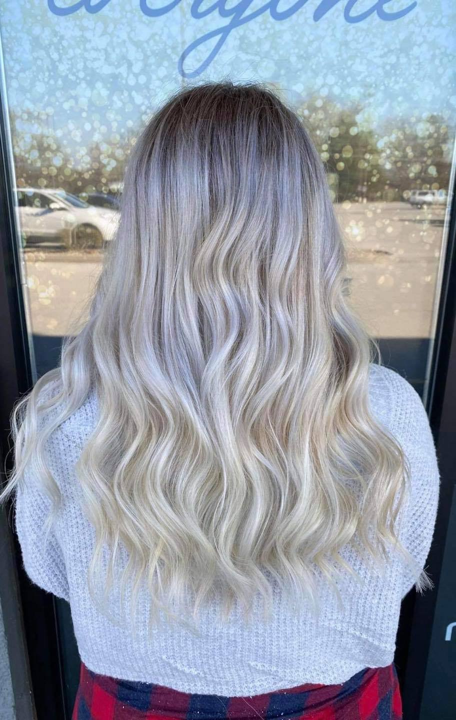 A woman with long blonde hair is standing in front of a window.