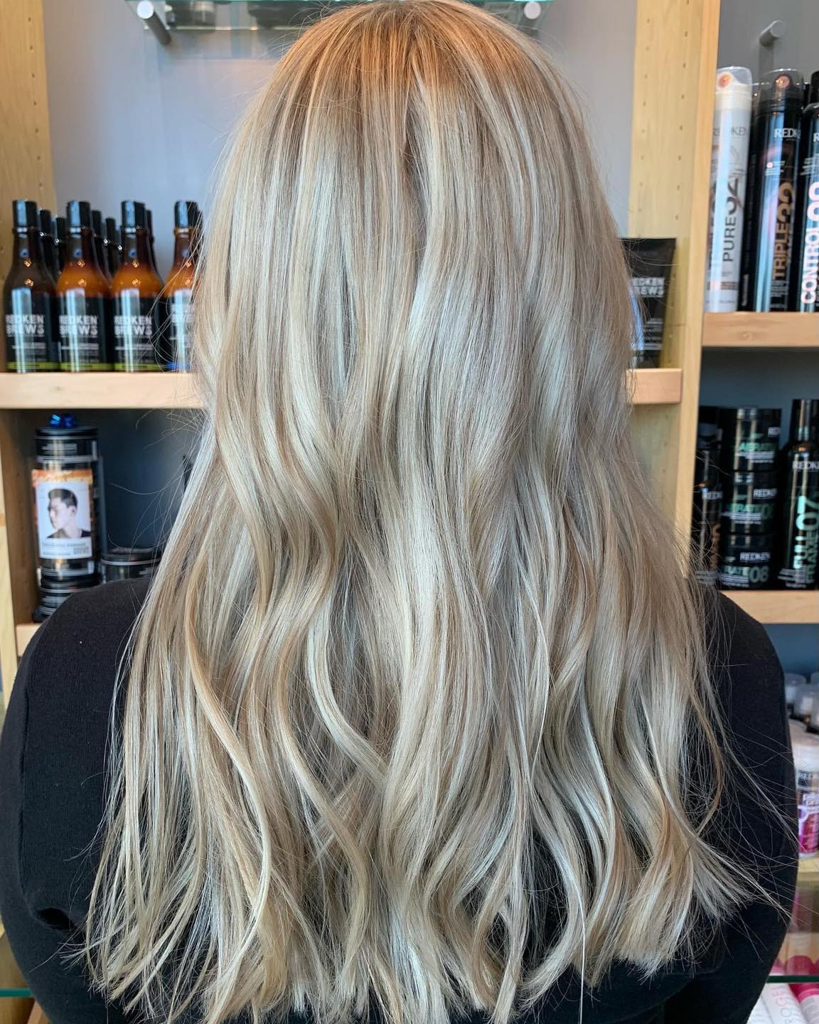 A woman with long blonde hair is standing in front of a shelf with bottles of hair products.