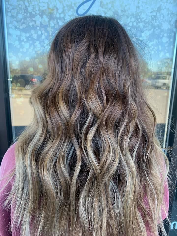 A woman with long wavy brown hair is standing in front of a window.
