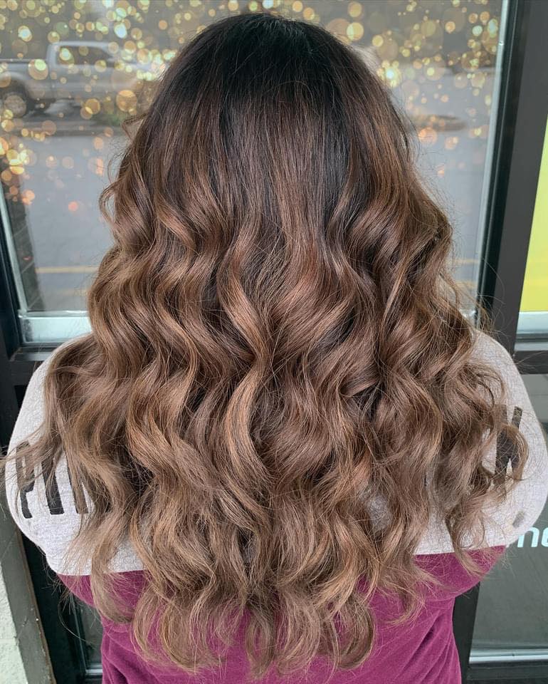 A woman with long wavy brown hair is standing in front of a window.
