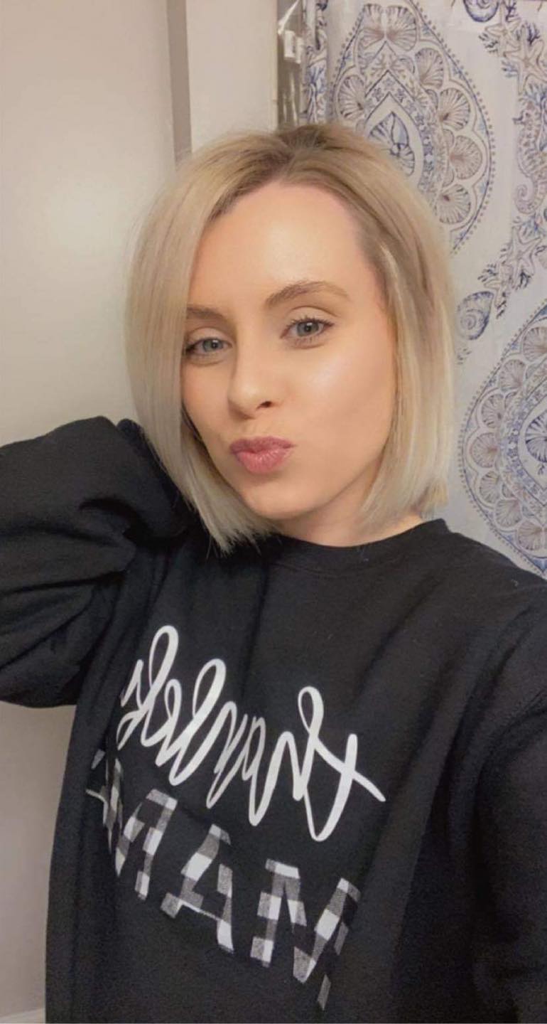 A woman is taking a selfie in a bathroom wearing a black sweatshirt.