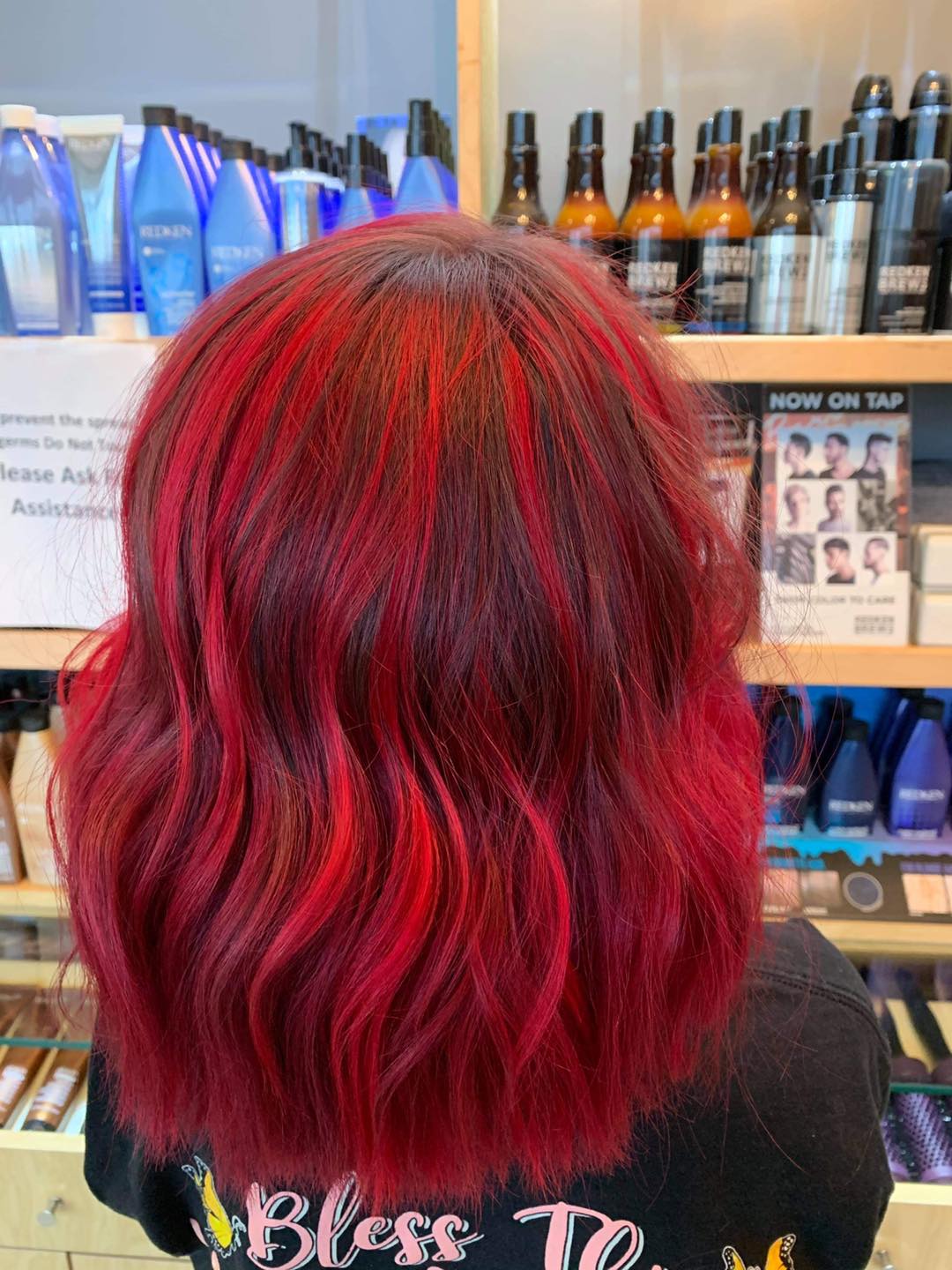 A woman with red hair is standing in front of a shelf of hair products.