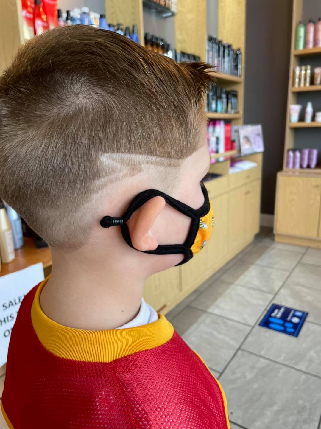 A young boy is wearing a mask in a hair salon.