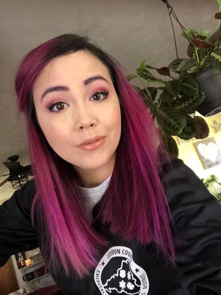 A woman with purple hair is taking a selfie in front of a plant.