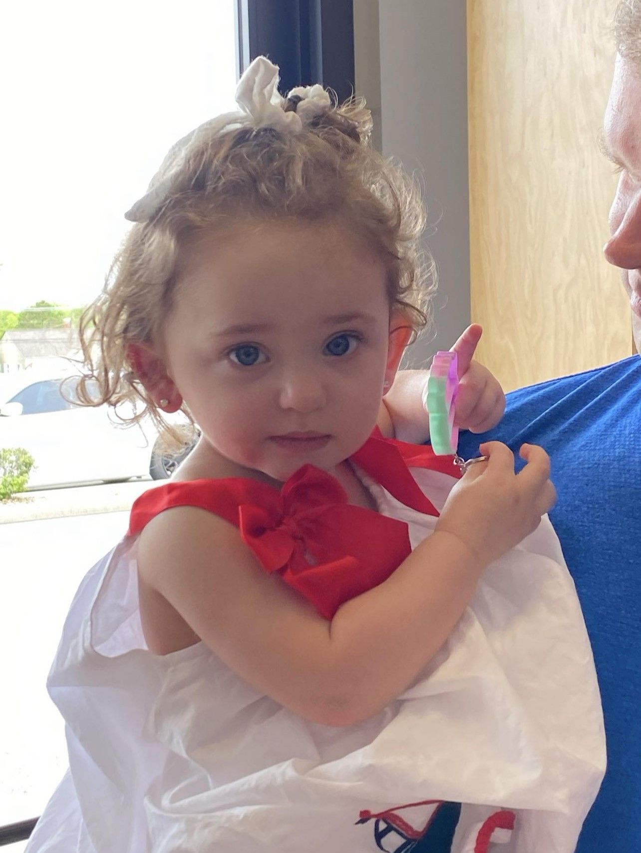 A little girl in a red and white dress is holding a toothbrush