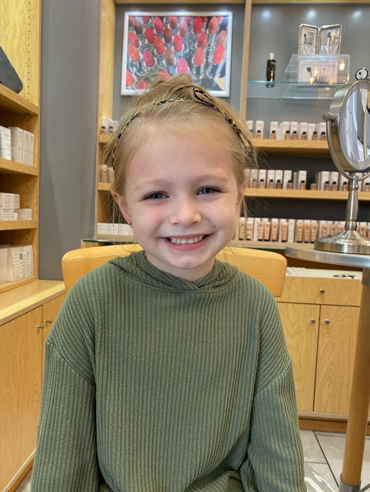 A little girl in a green sweater is smiling in a store.