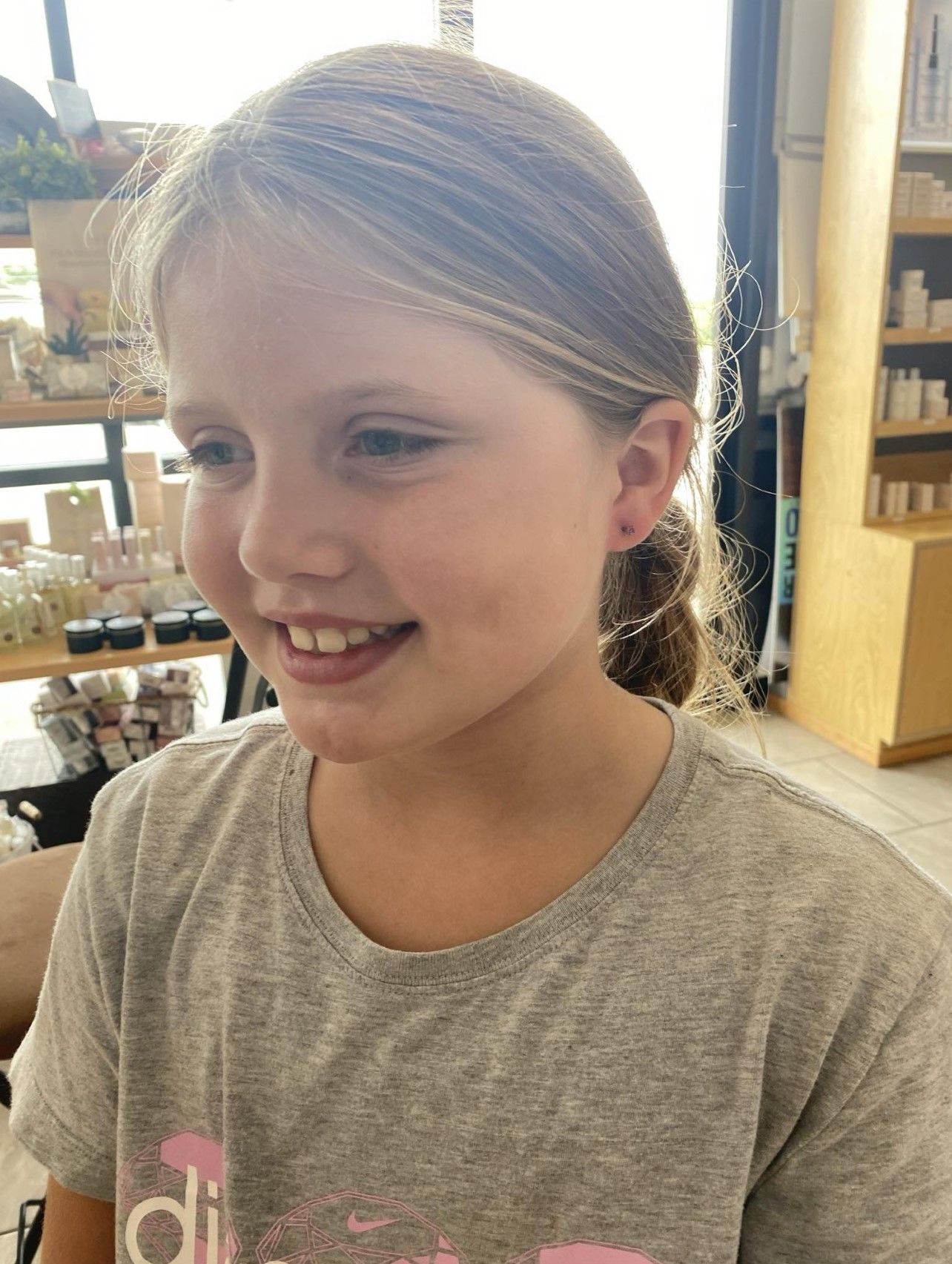 A young girl wearing a gray shirt is smiling in a store.
