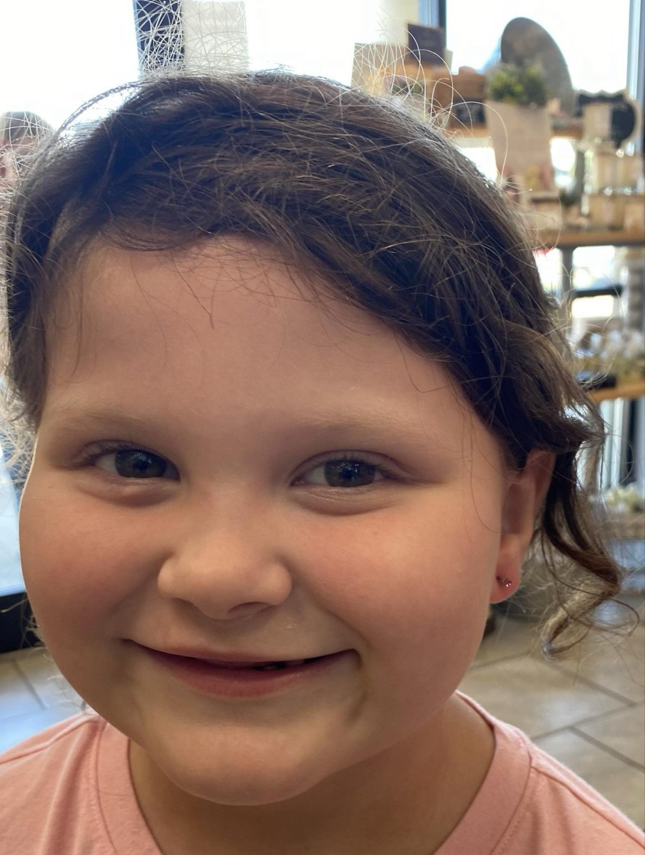 A little girl wearing a pink shirt is smiling for the camera.