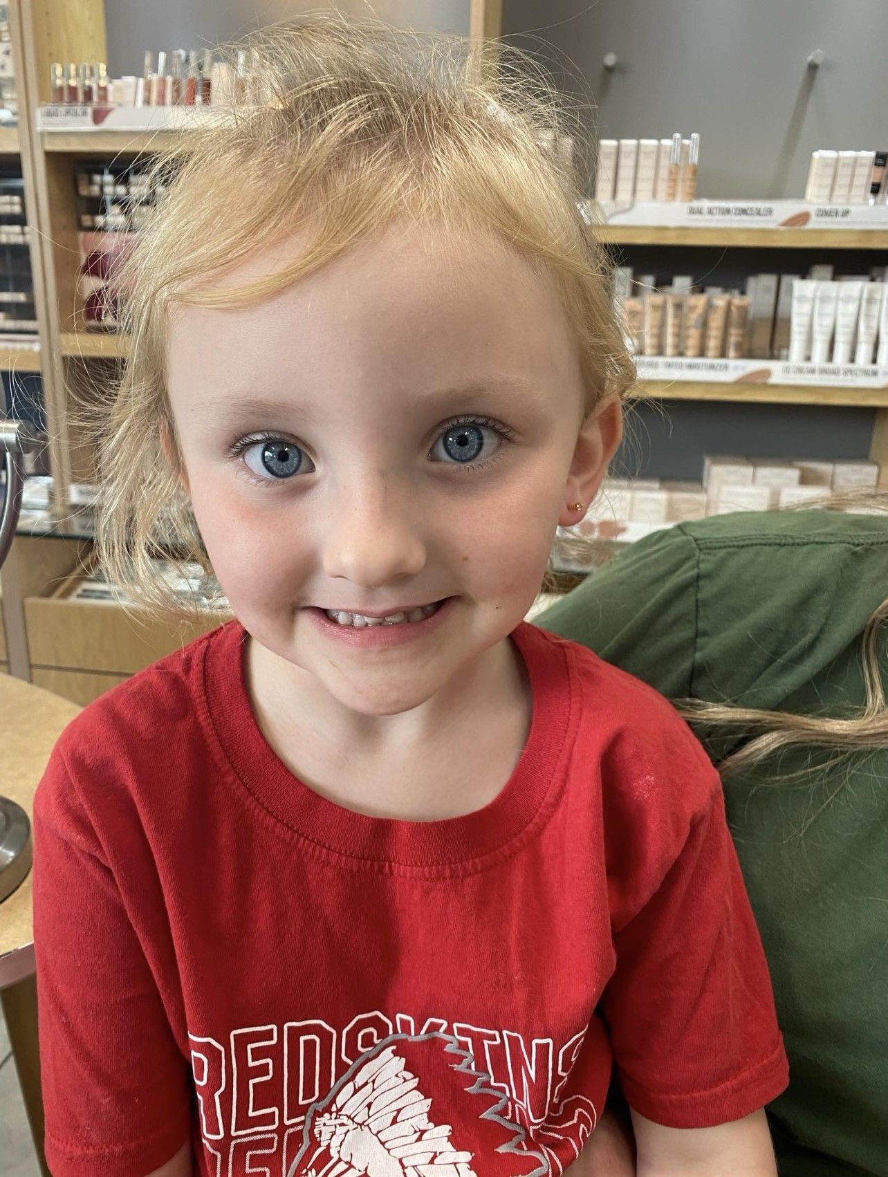 A little girl wearing a red shirt with the word reds on it