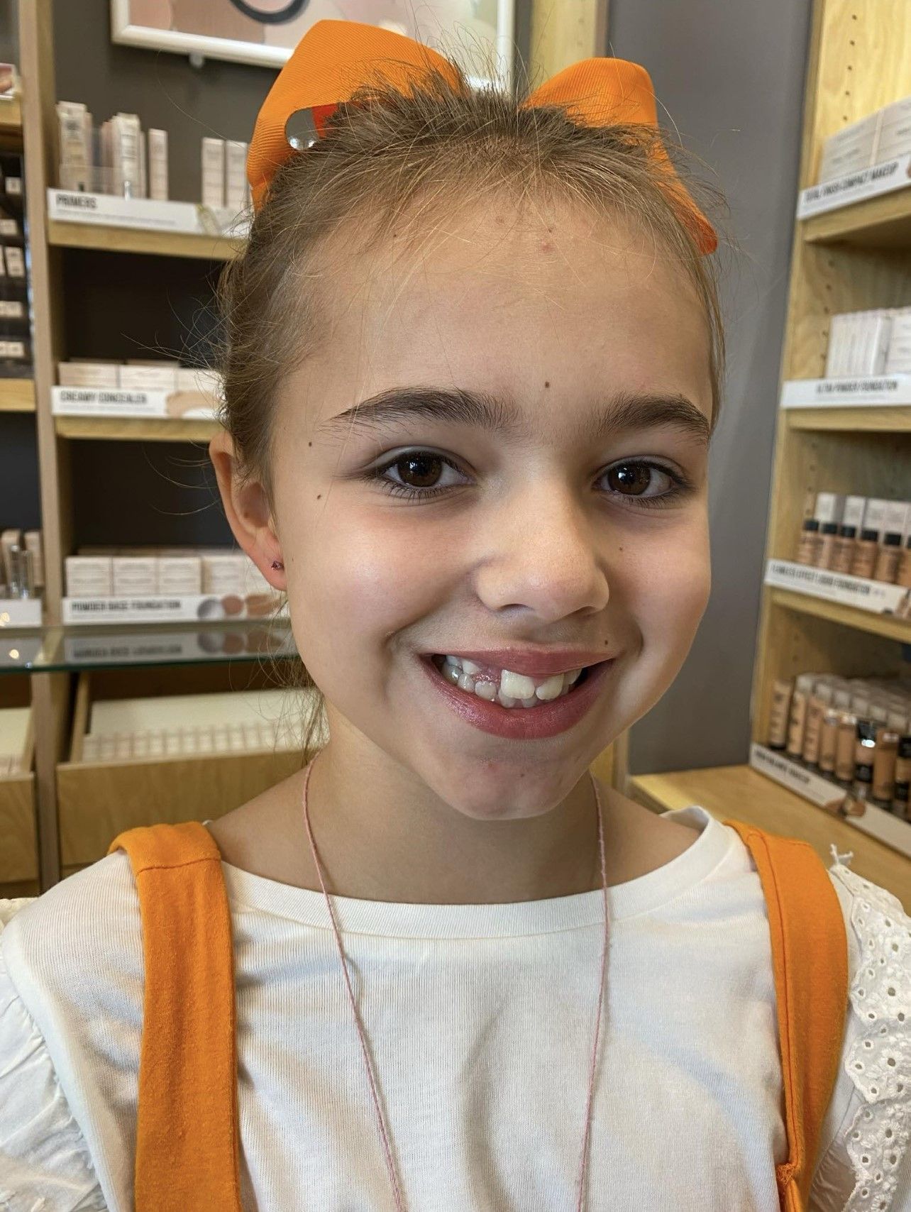 A young girl with a bow in her hair is smiling in a store.