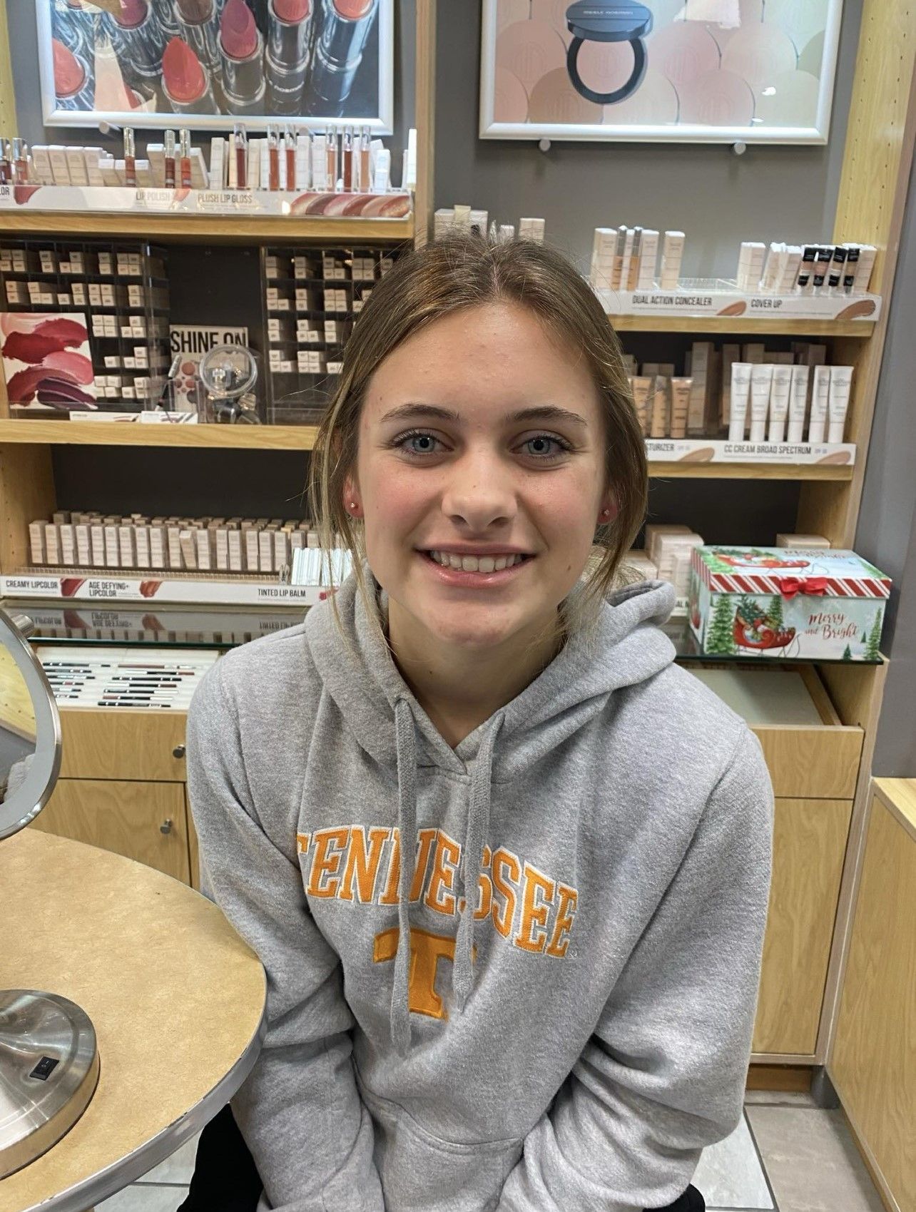 A young woman wearing a gray hoodie is smiling in a store.