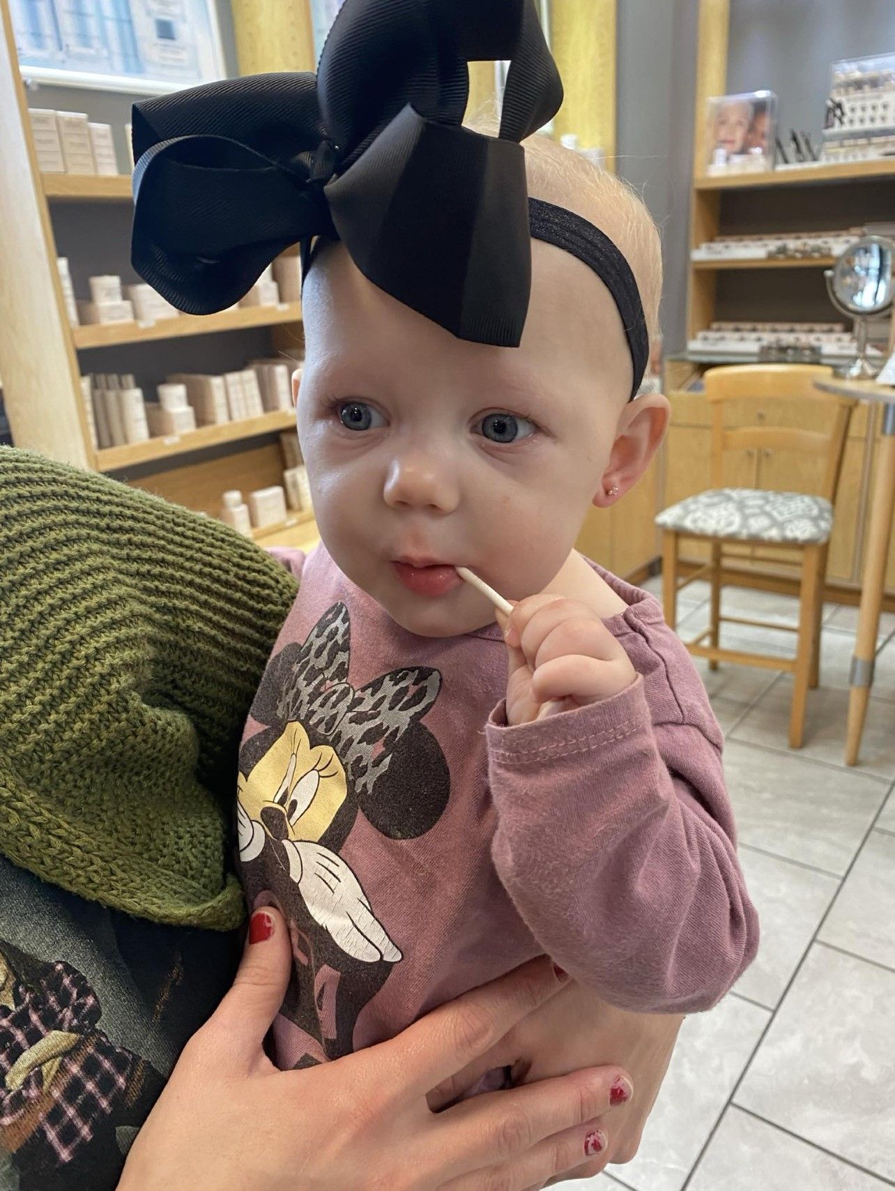 A baby with a black bow on her head is eating a toothpick.