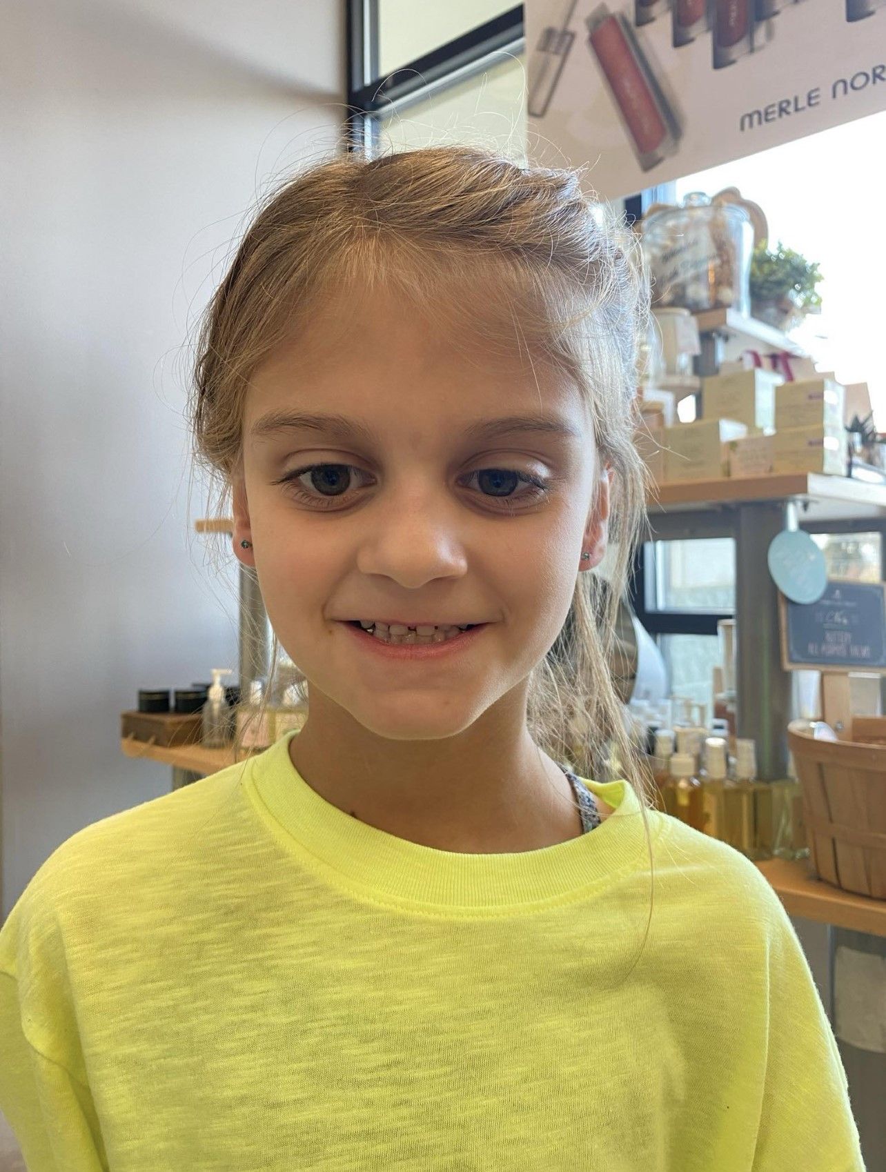 A young girl wearing a neon yellow sweater is smiling in a store.