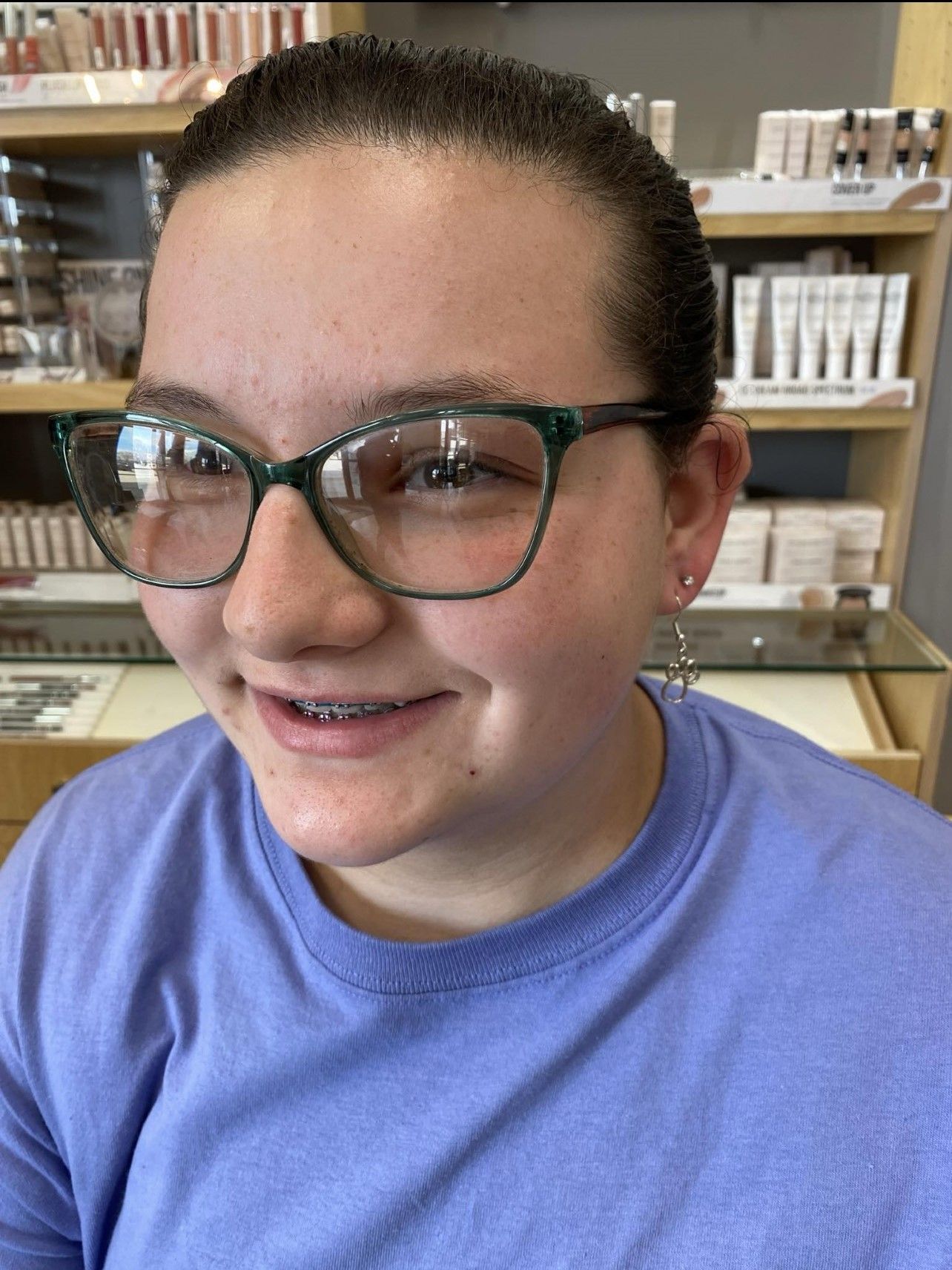A woman wearing glasses and a purple shirt is smiling.