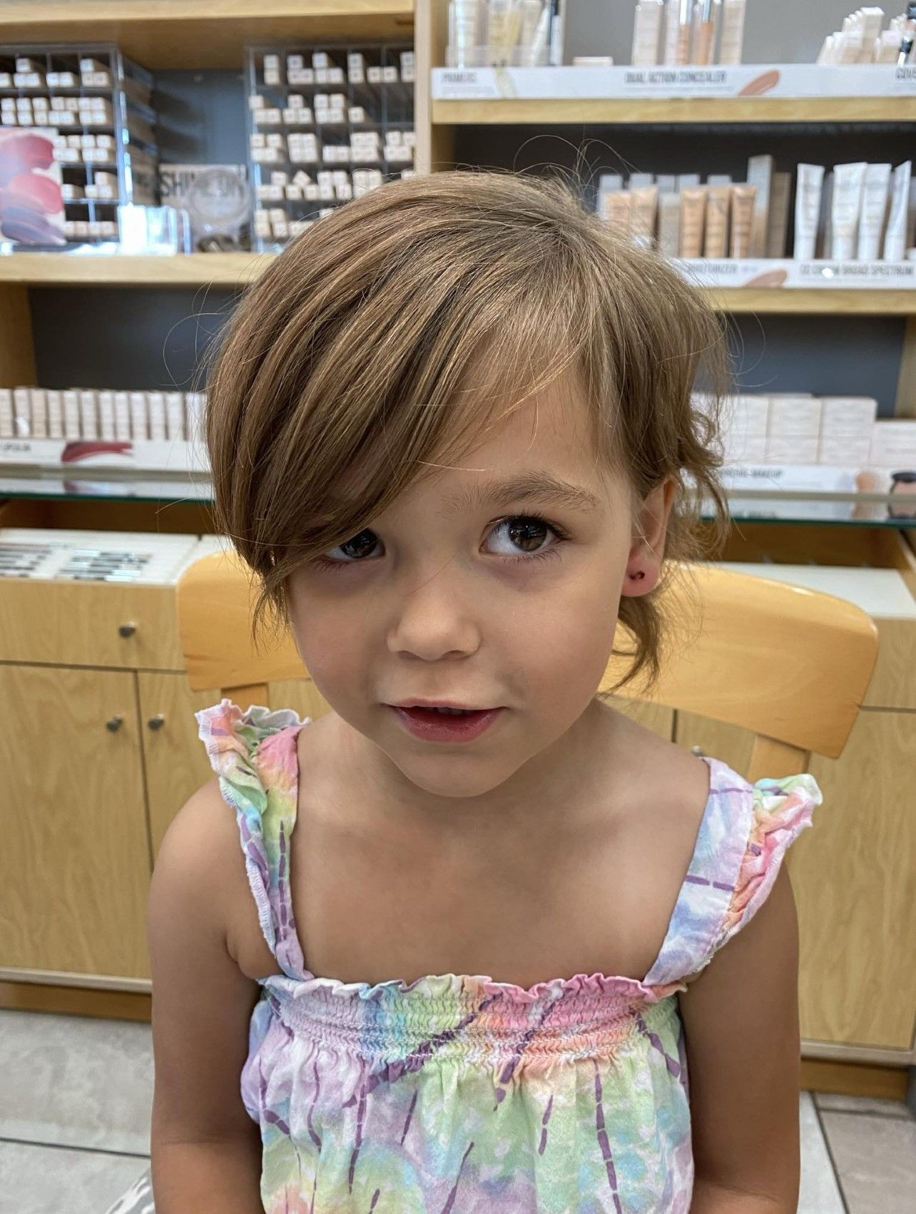 A little girl is sitting in a chair in a store looking at the camera.