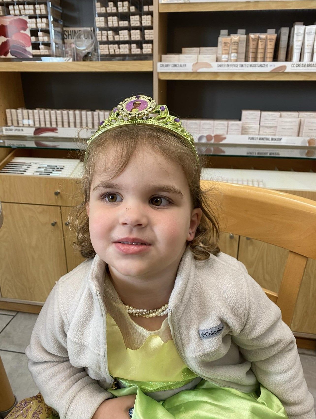 A little girl wearing a tiara and a dress is sitting in a chair