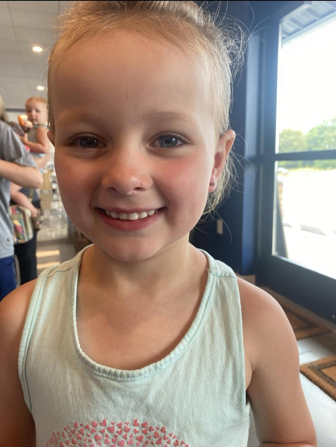 A little girl in a tank top is smiling for the camera
