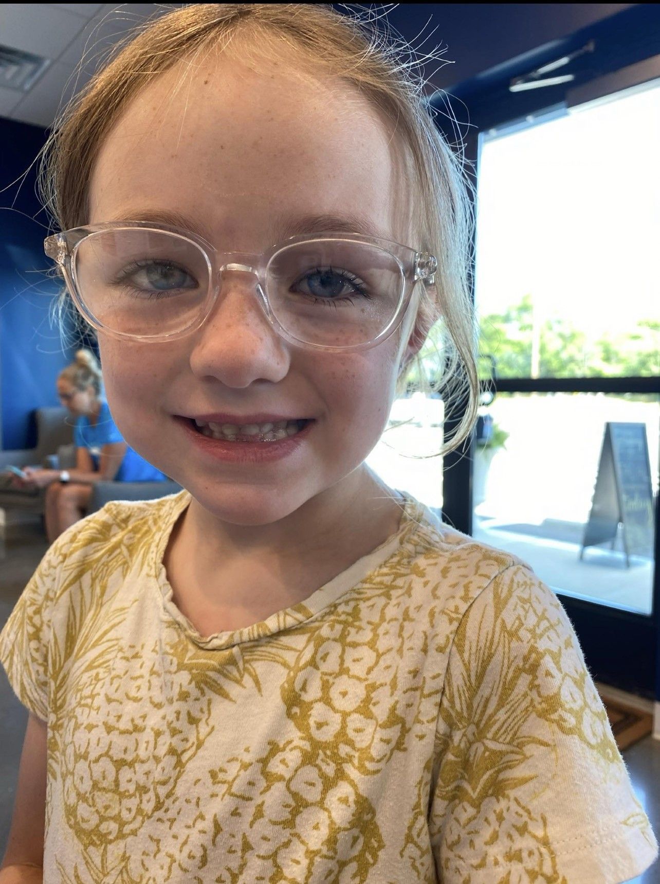 A young girl wearing glasses and a pineapple shirt is smiling for the camera.