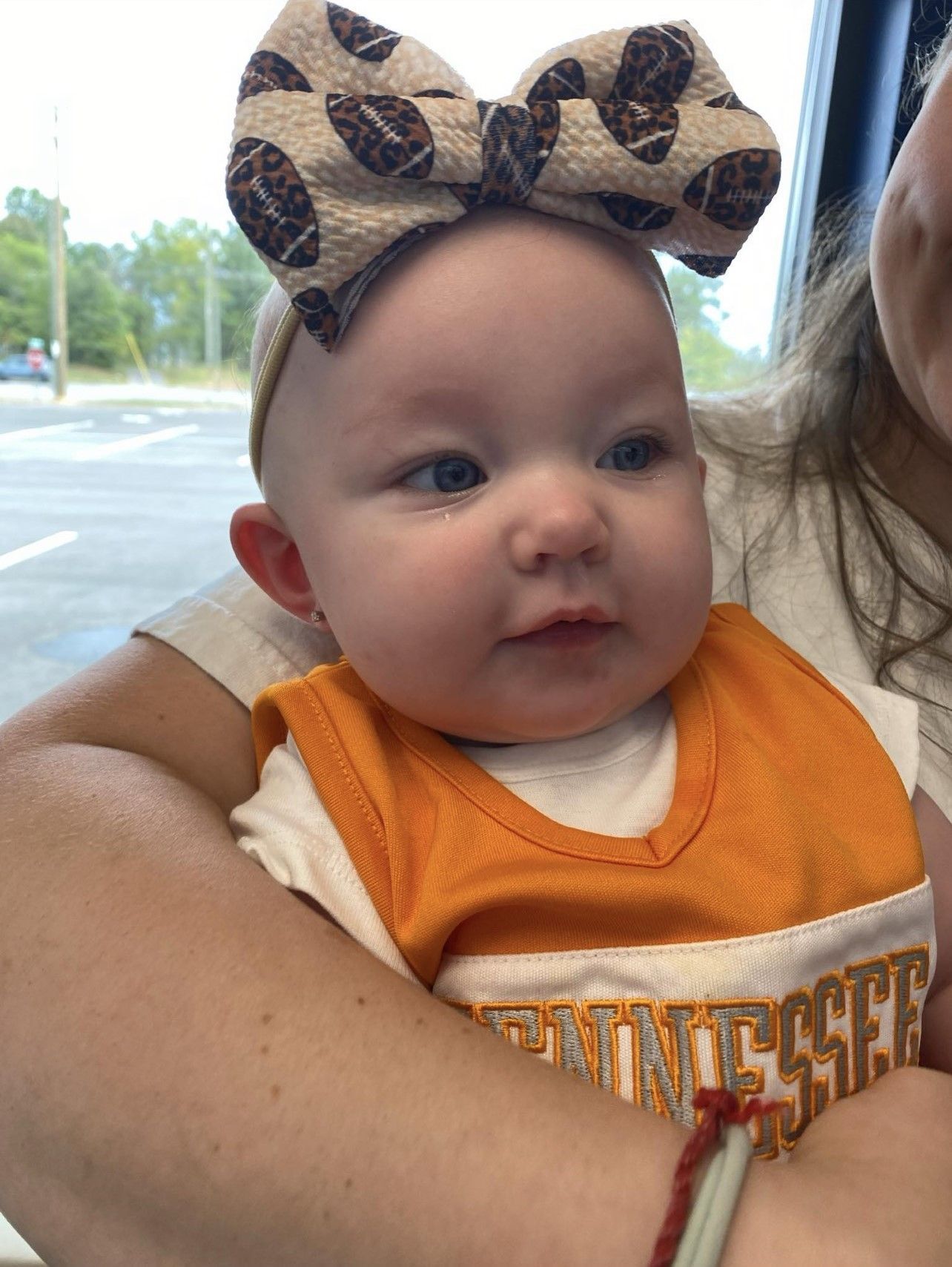 A baby with a bow on her head is being held by a woman.