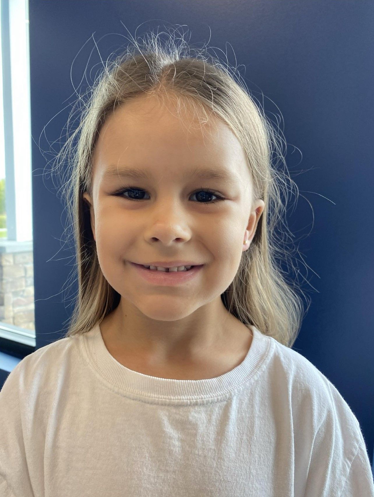 A young girl wearing a white shirt is smiling for the camera.
